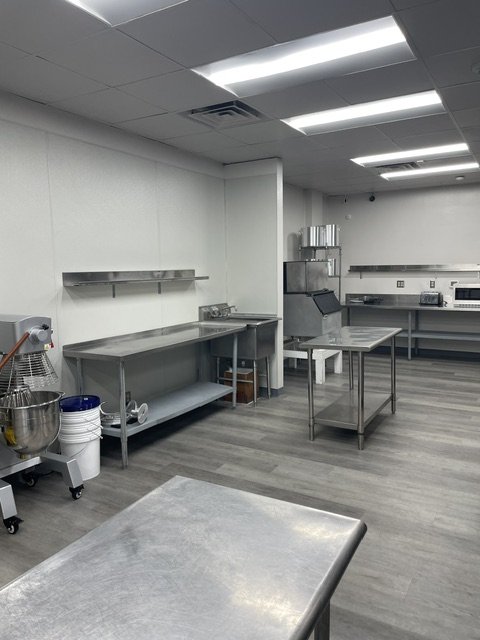 Empty commercial kitchen with stainless steel tables, shelves, and commercial kitchen equipment.