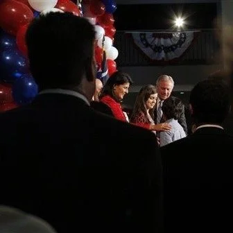 People dressed in formal attire at an indoor event with red, white, and blue balloon decorations.
