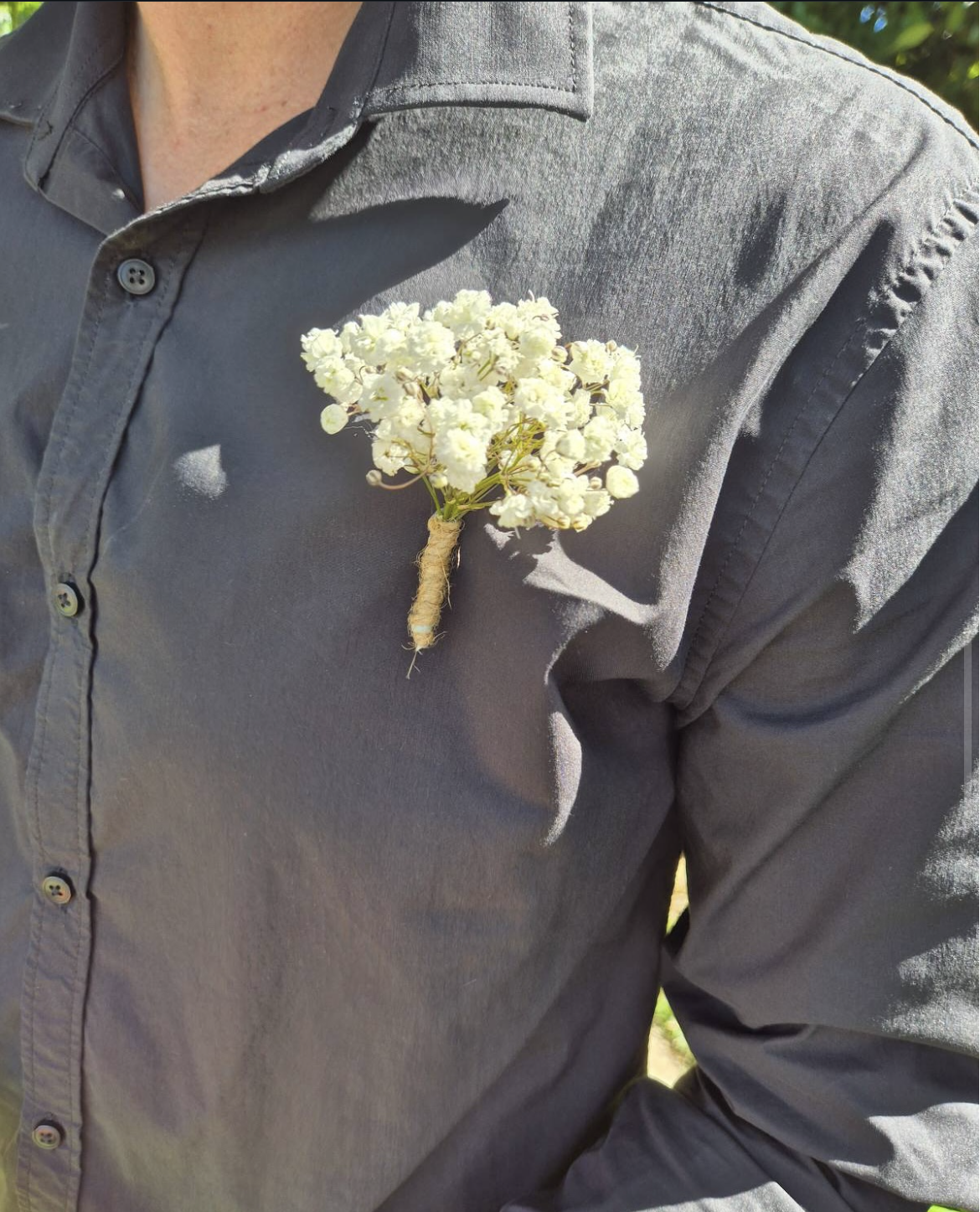 A person wearing a gray shirt has a small bouquet of white flowers pinned to the chest.