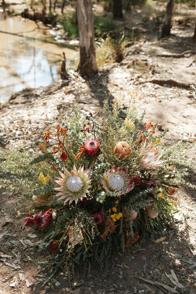 A bouquet of native Australian flowers on the ground near a creek in the forest.