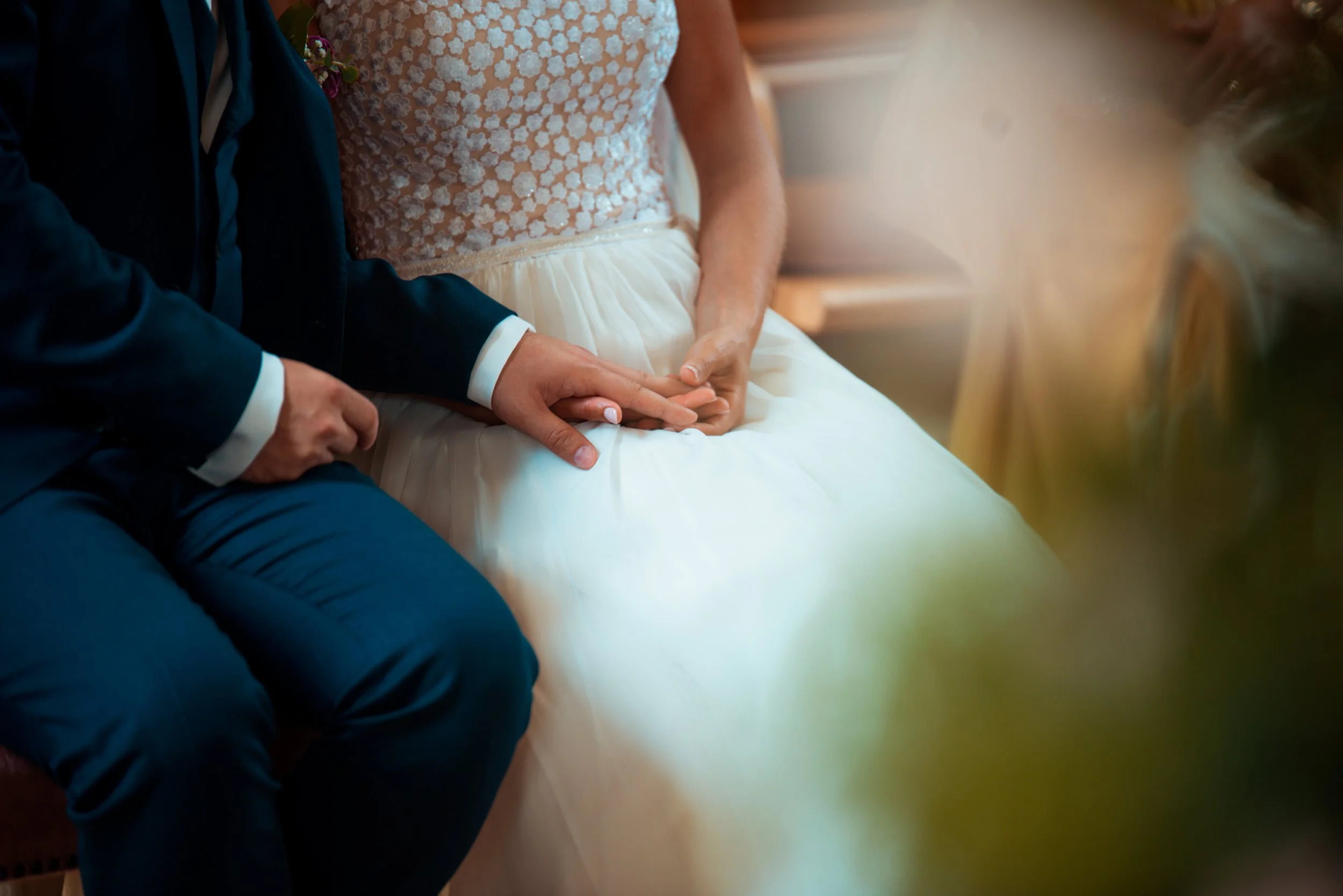 Nahaufnahme eines Brautpaares, das bei einer Hochzeit Händchen hält, mit Fokus auf die Hände.