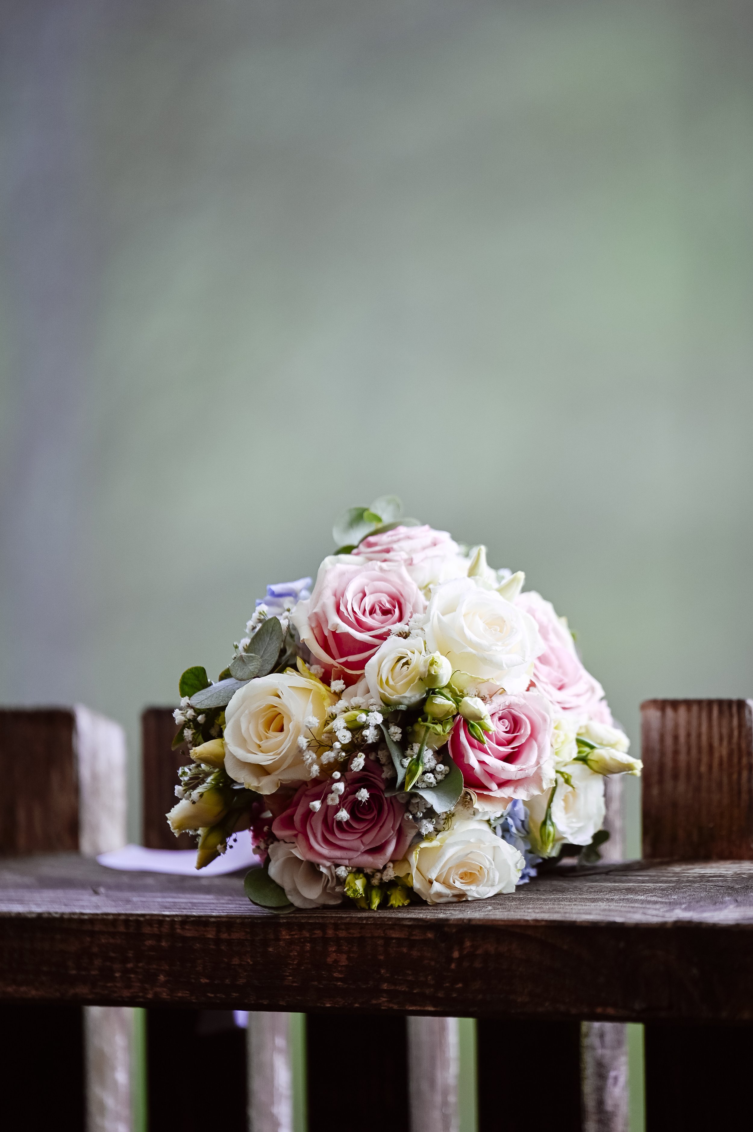 Ein Blumenstrauß aus weißen, rosa und lila Rosen, auf einem Holzscheibtisch vor einem grauen Hintergrund.
