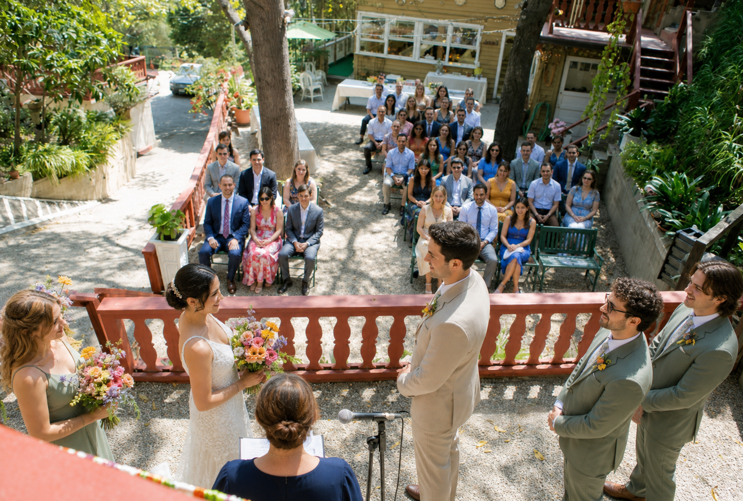 Outdoor wedding ceremony at Nature Friends Los Angeles, with a couple exchanging vows on a rustic garden terrace overlooking seated guests, trees, flowers, and the historic clubhouse setting.