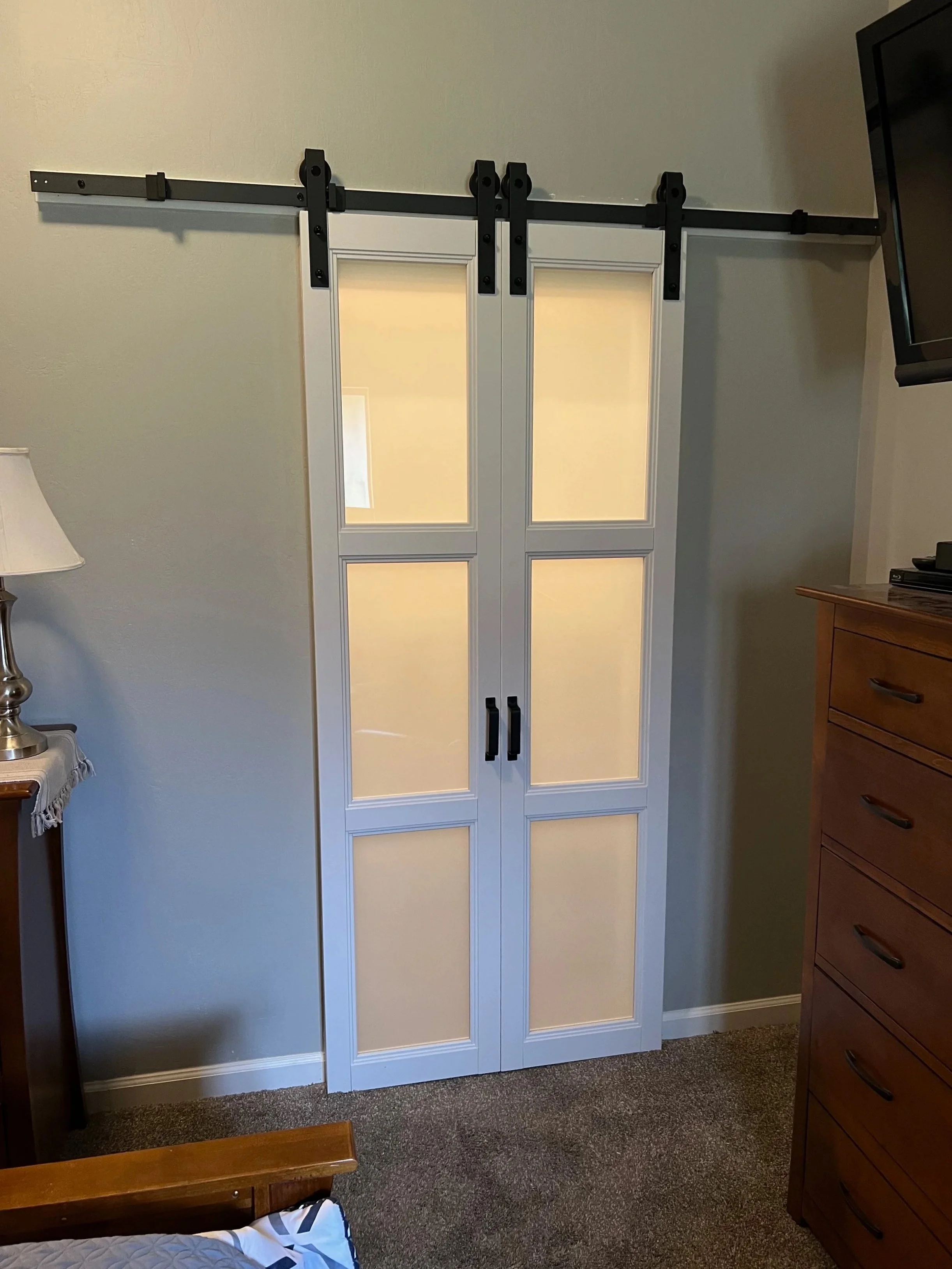 White double barn doors with black handles and black sliding hardware mounted above on a wall in a room.