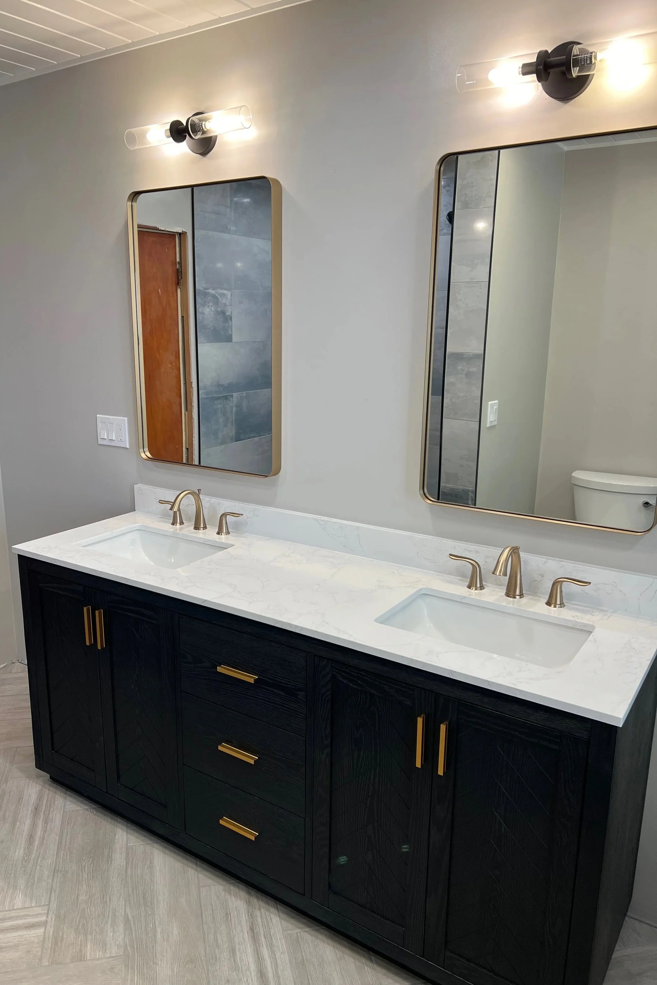 Modern bathroom vanity with a marble countertop, gold hardware, and two rectangular mirrors above two sinks, with wall-mounted light fixtures.