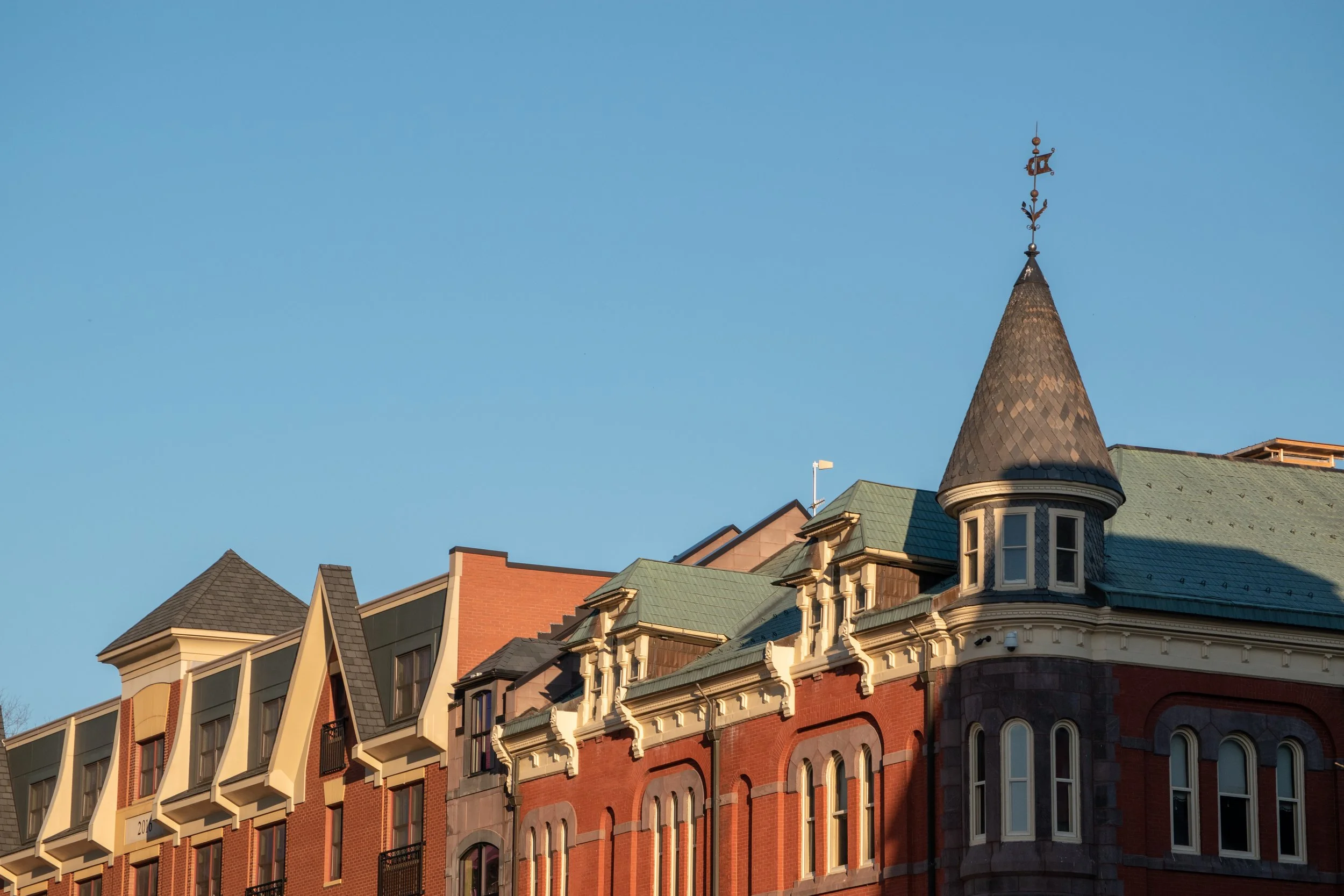 Close-up of a historic brick building with ornate architectural details, pointed turret, and multiple windows against a clear blue sky.