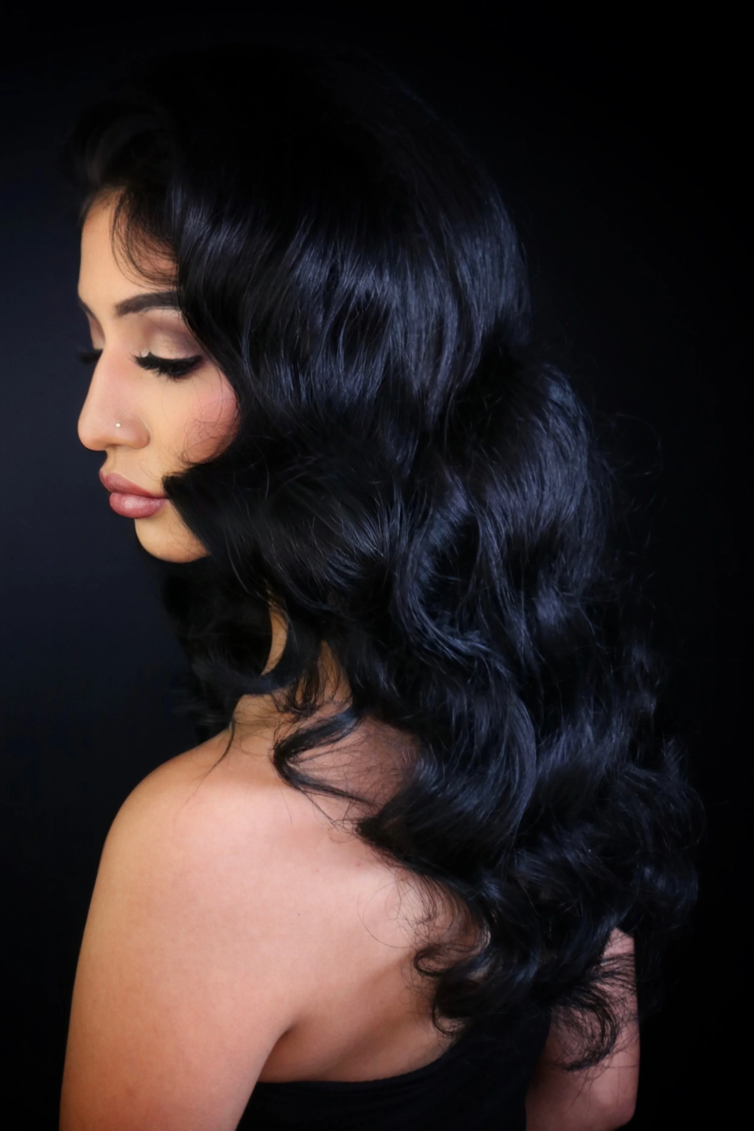 Side profile of a woman with long, wavy, black hair against a dark background.