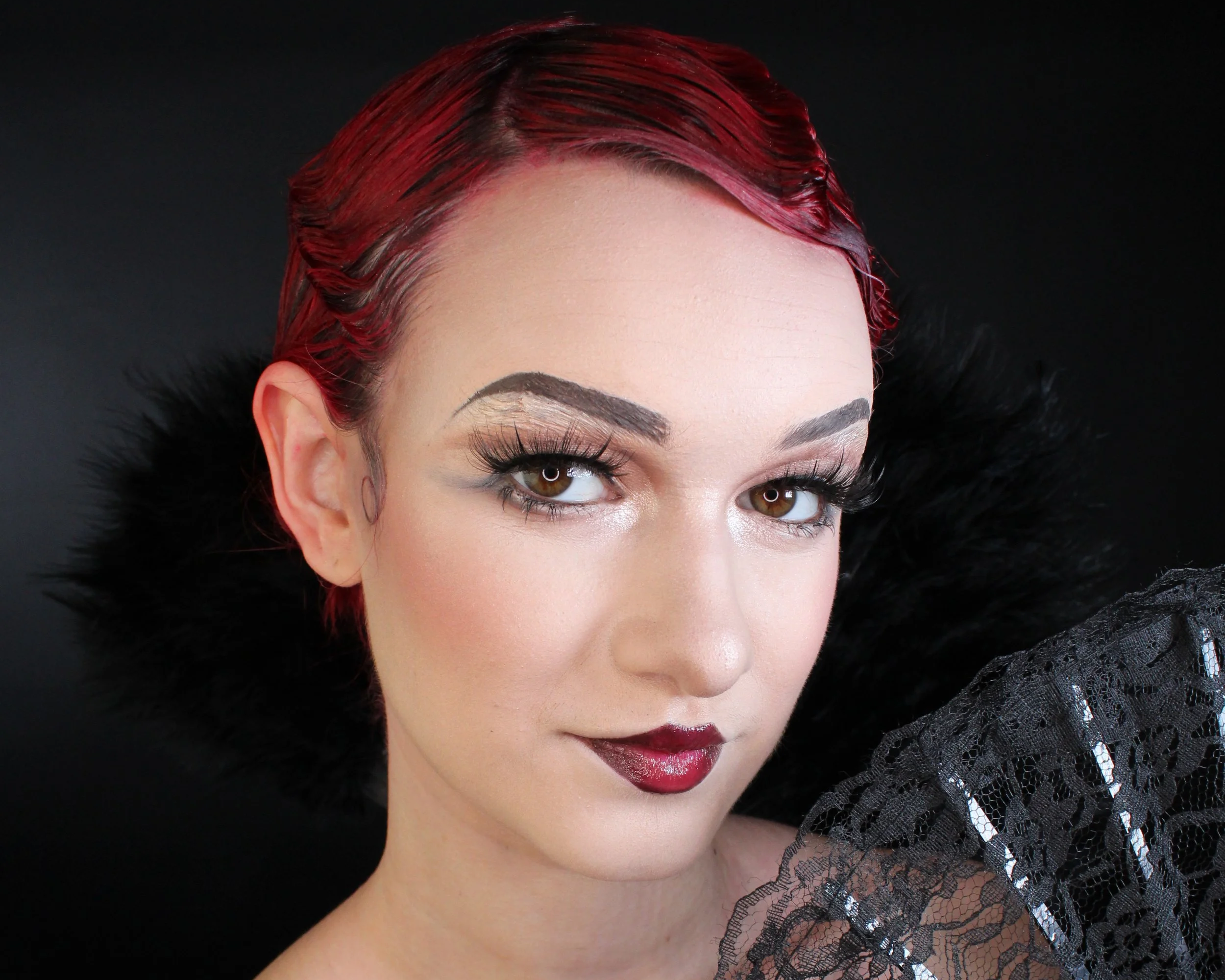 A woman with red hair, makeup, wearing a black fur collar and black lace garment, looking at the camera.