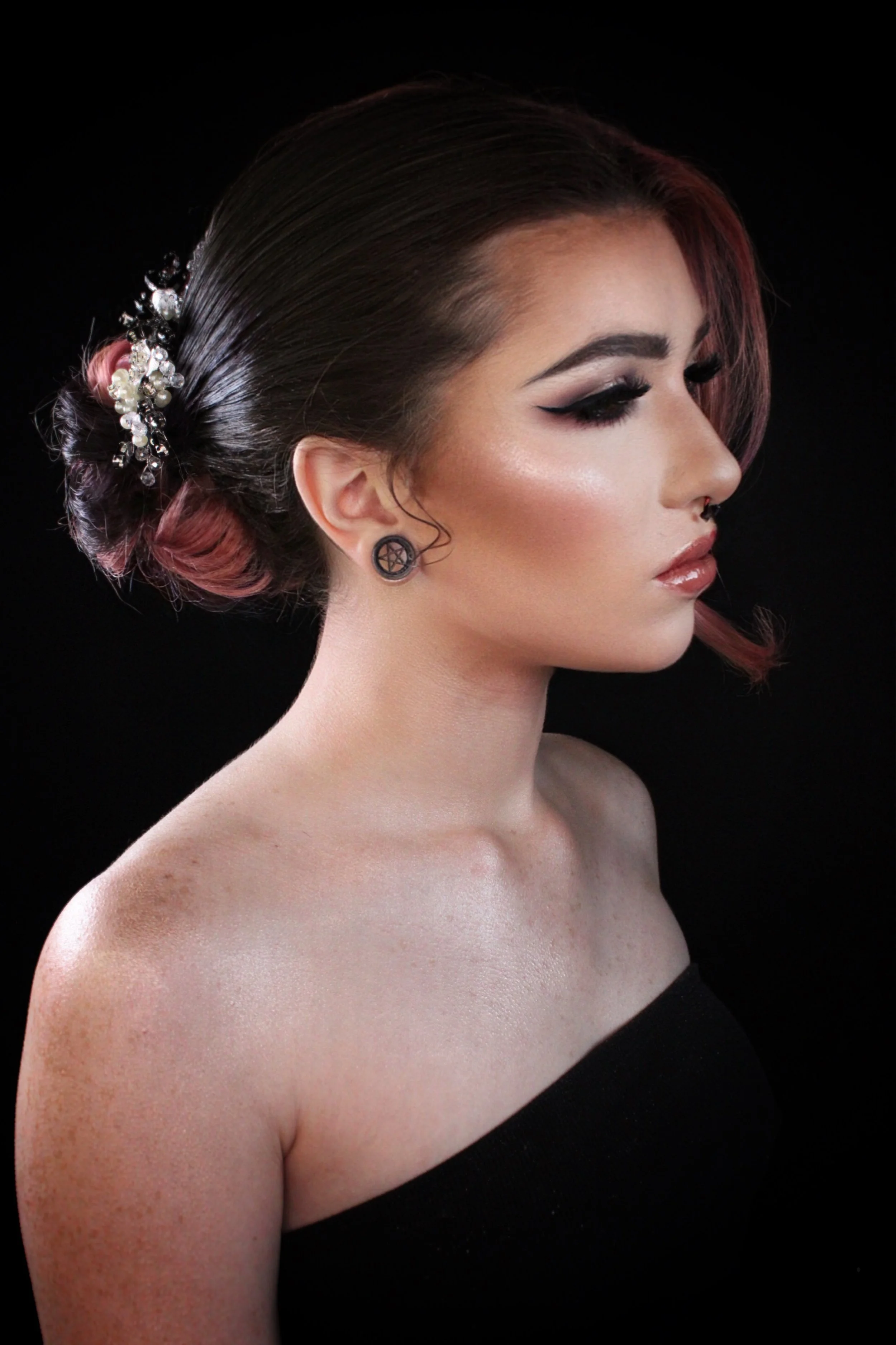 Side profile of a woman with styled hair, makeup, and pentagram earrings, against a black background.