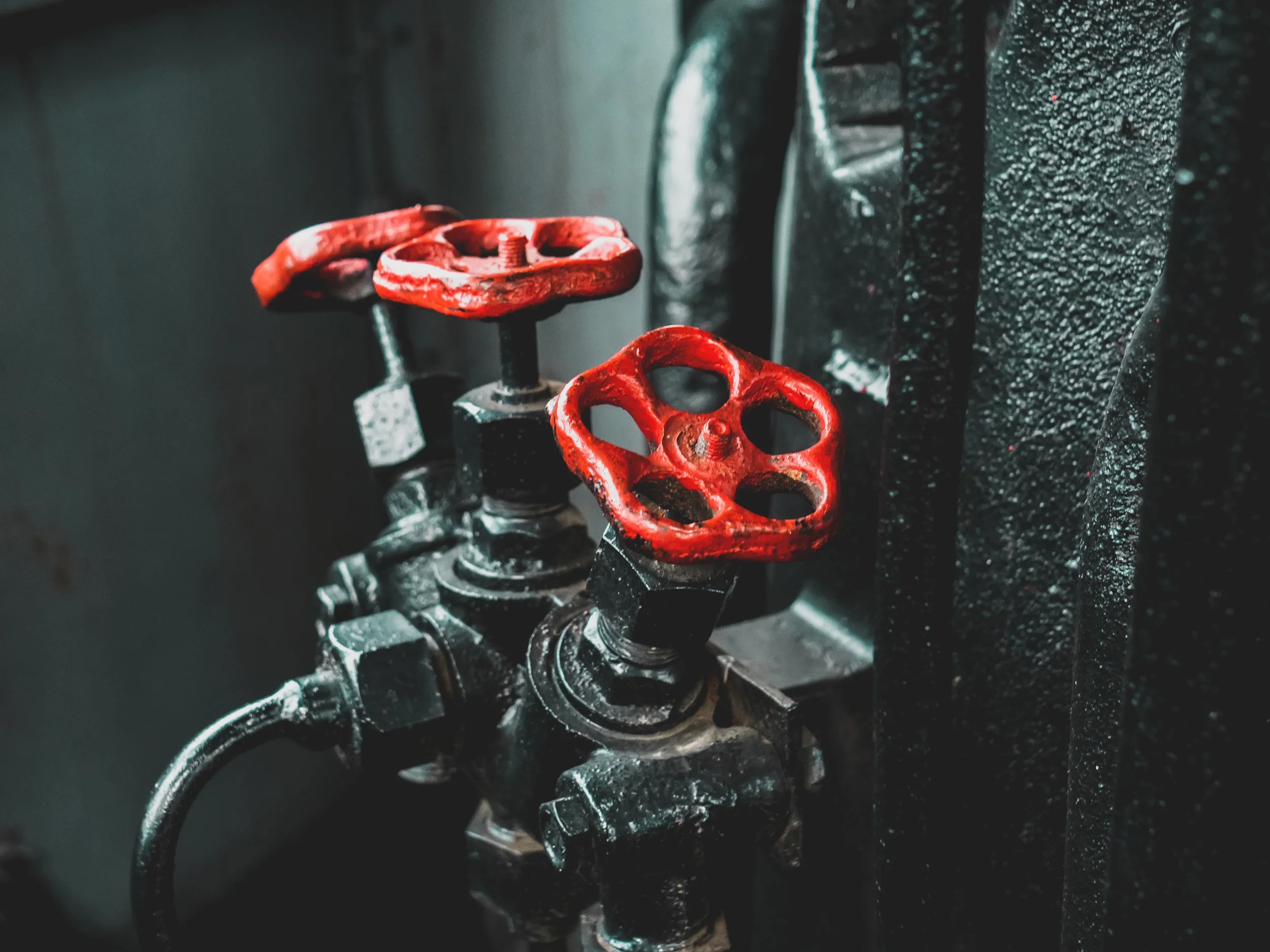 Close-up of two red wheel valves on a black industrial pipe or machinery, with textured black surface.