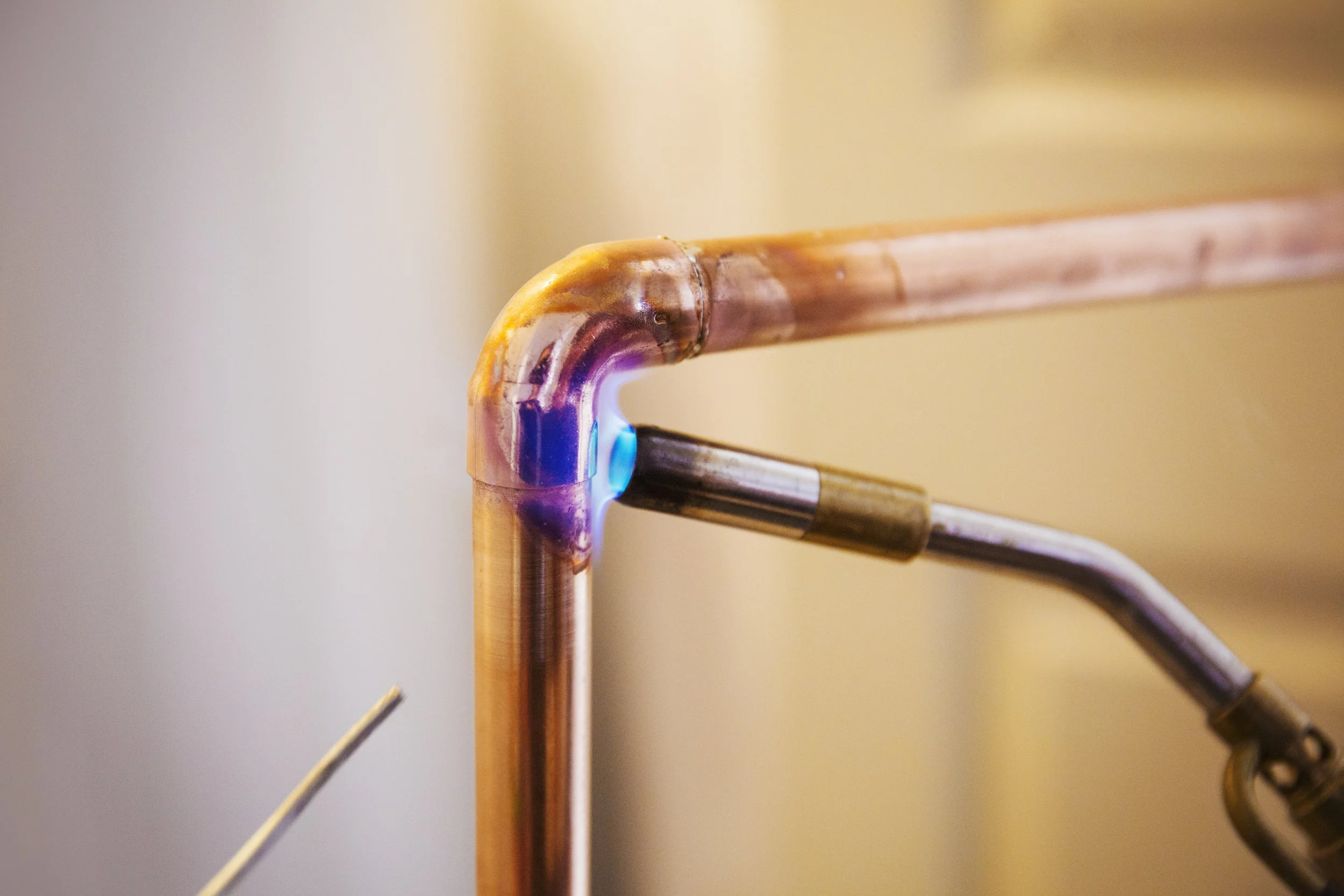 Close-up of a copper pipe with a welding joint and a blue arc from welding equipment.