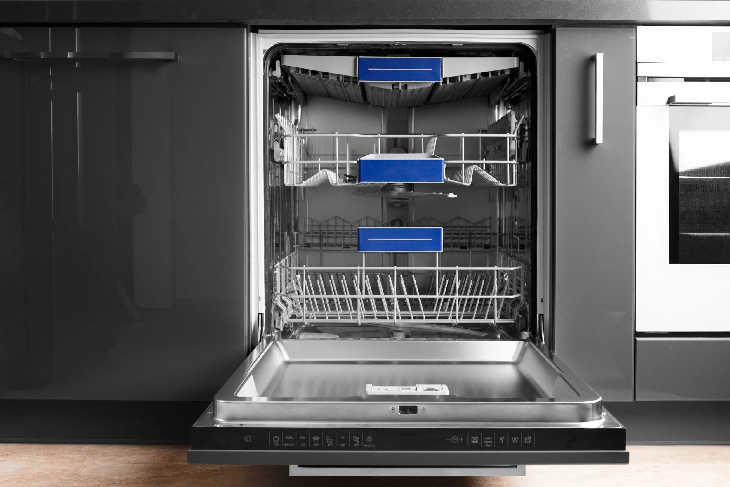 Open dishwasher with empty racks, built into kitchen cabinetry.