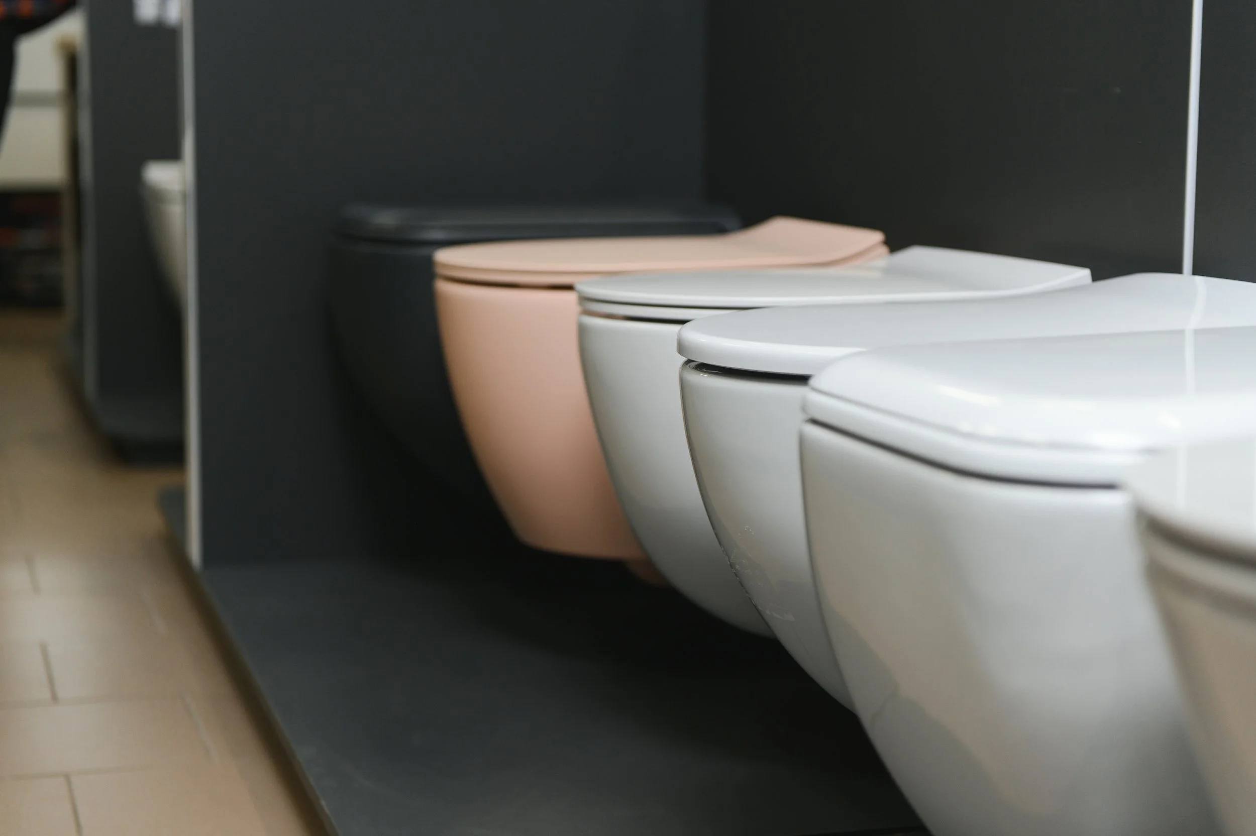 Row of modern toilets in a bathroom display with black, pink, white, and cream colors.