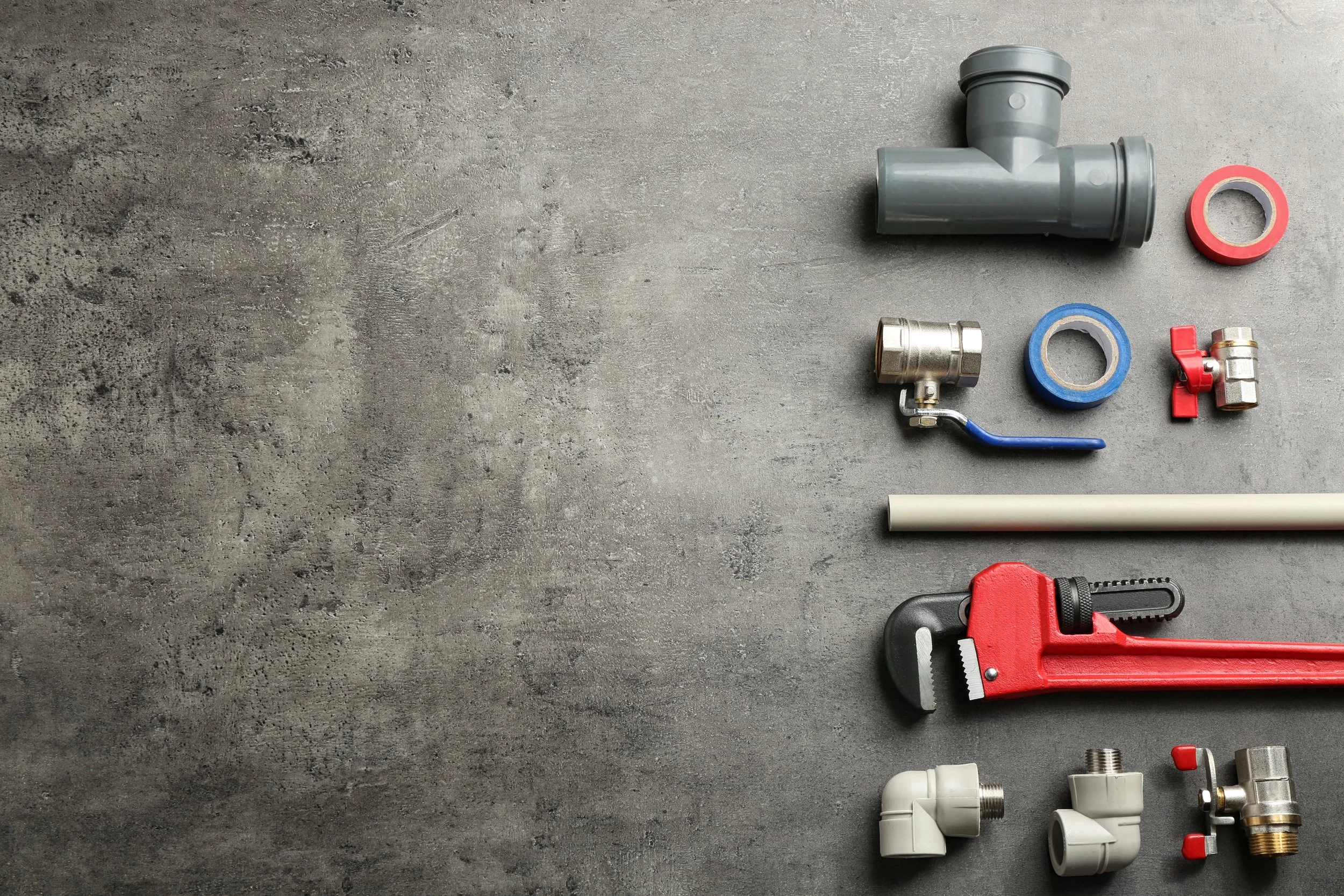 Various plumbing parts including pipes, fittings, and a pipe cutter tool arranged on a concrete surface.