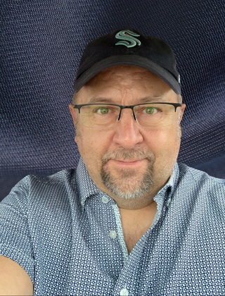 A man with glasses, a beard, and a cap taking a selfie.