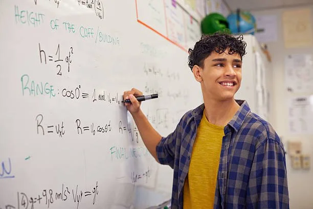 A teenage boy writing math equations on a classroom whiteboard.