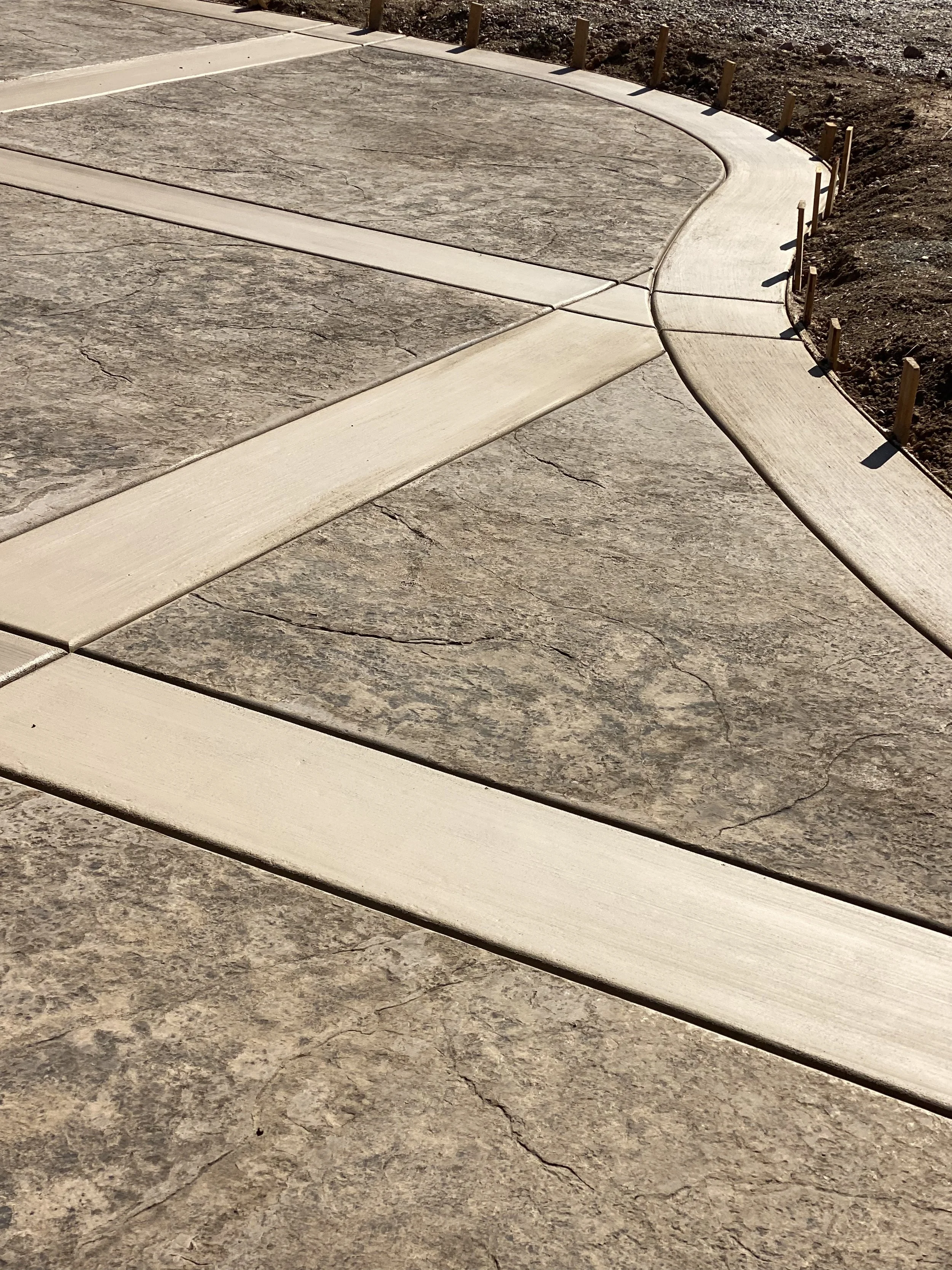 Curved concrete sidewalk with wooden posts along the edge on a sunny day.