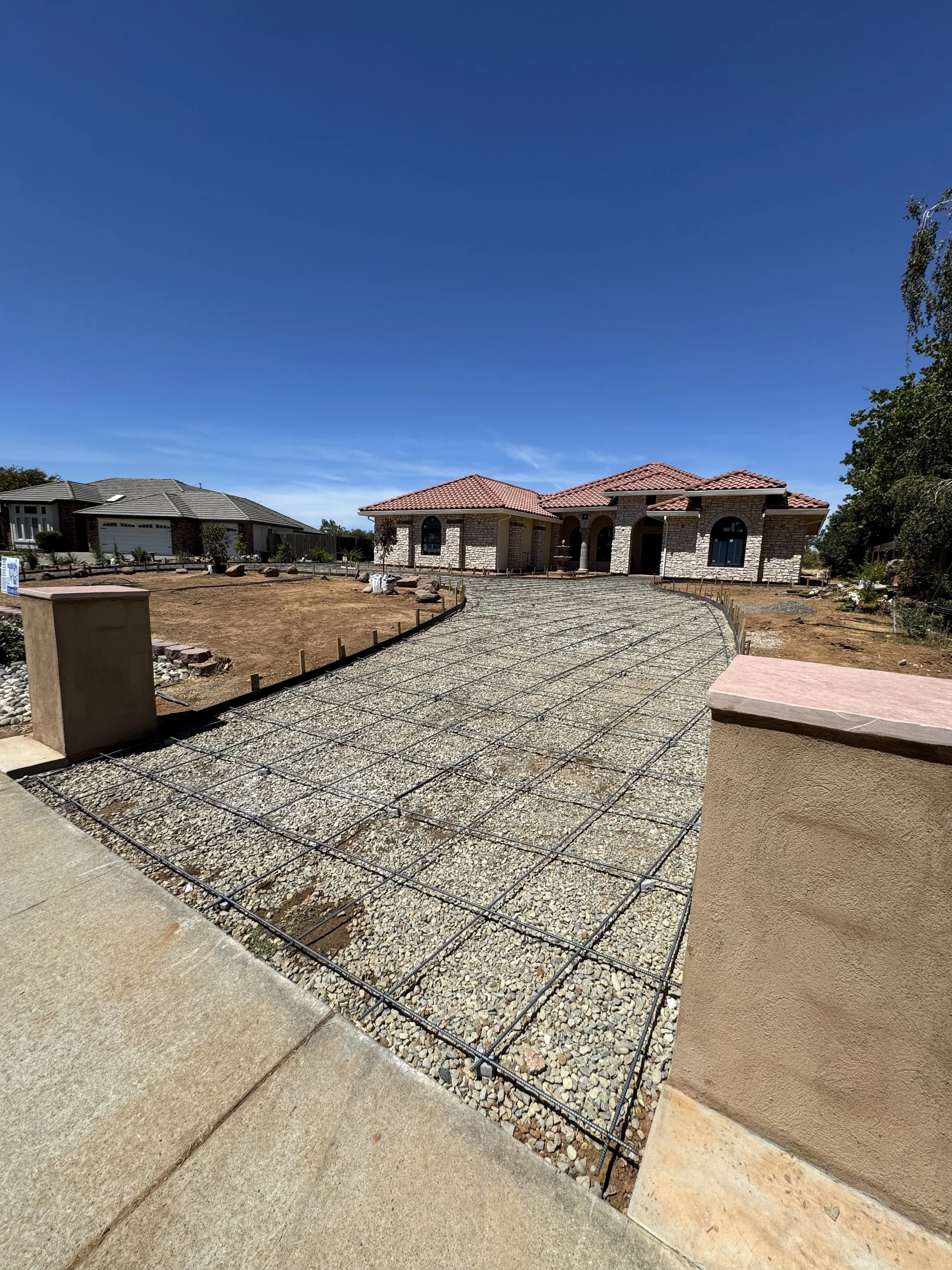 Construction site of a driveway with gravel and rebar in front of a house with a tiled roof.