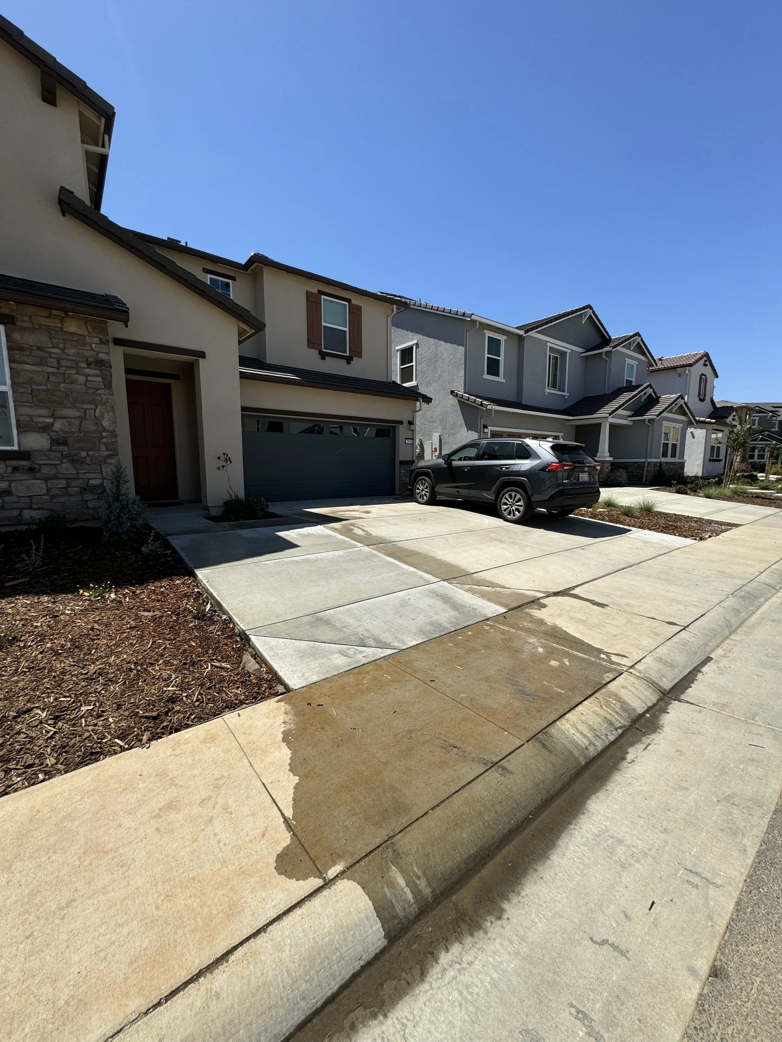 Residential houses with a driveway, parked car, and a clear blue sky.