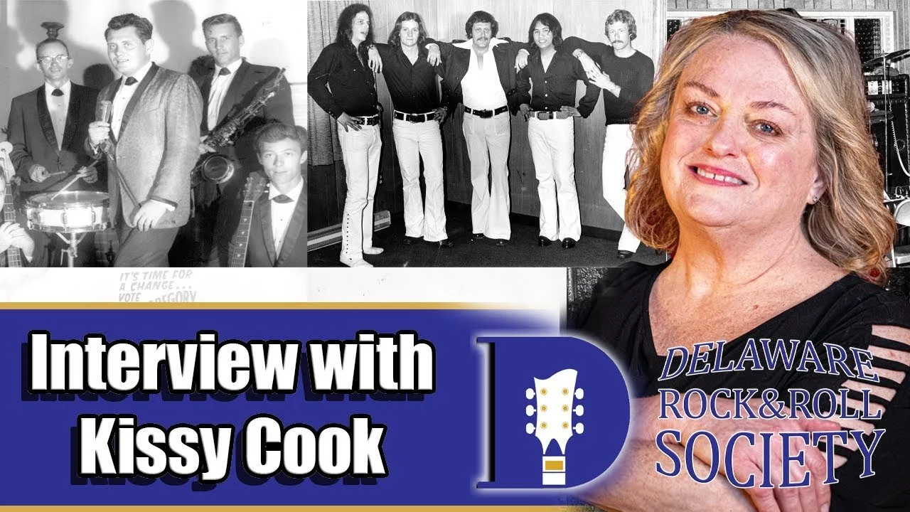 A collage of three photos. The top left is a black-and-white photo of a band with a young man holding a drink and a saxophone, and a young boy in front. The top right is a black-and-white photo of five women and one man standing together, dressed in vintage-style clothing. The bottom right is a colored photo of a smiling middle-aged woman with shoulder-length light brown hair, wearing a black top with cut-out shoulders, positioned in front of a background featuring the Delaware Rock & Roll Society logo. The bottom left has text that reads 'Interview with Kissy Cook' against a blue background, with a white and blue guitar icon and the Delaware Rock & Roll Society text.