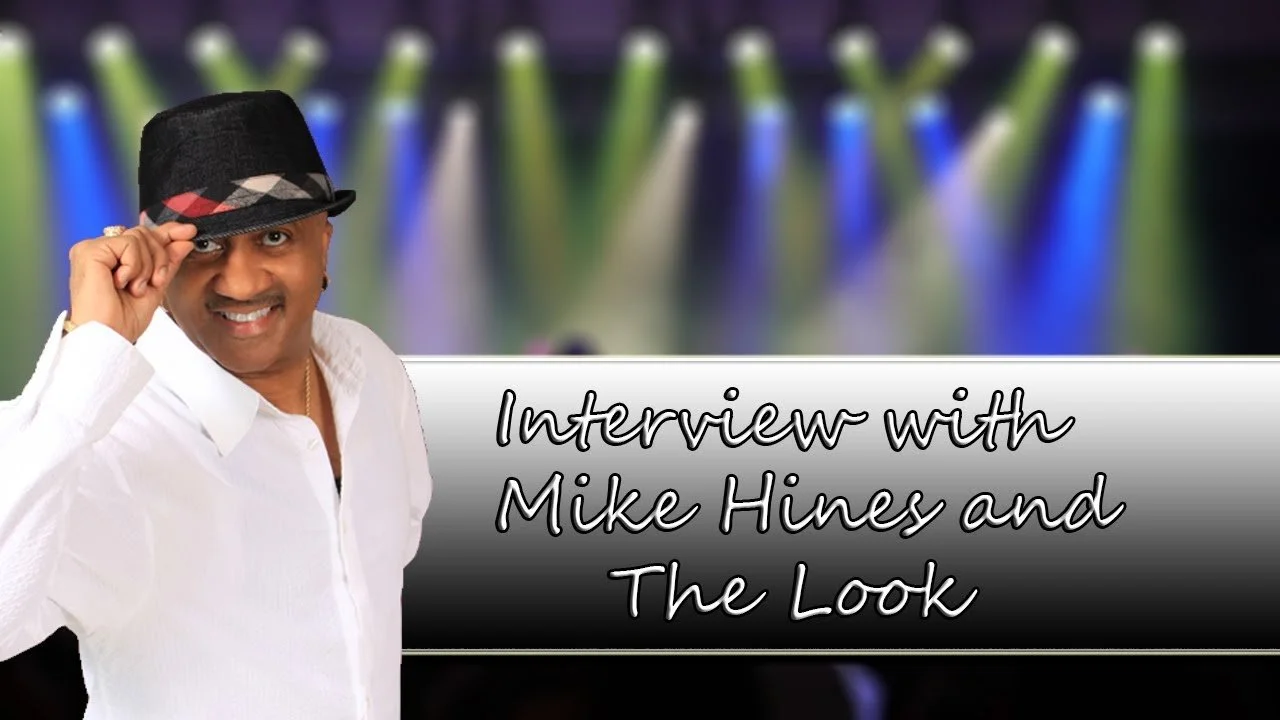 A man in a white shirt and black hat posing in front of a stage background with colorful lights, with the text 'Interview with Mike Hines and The Look' overlayed.