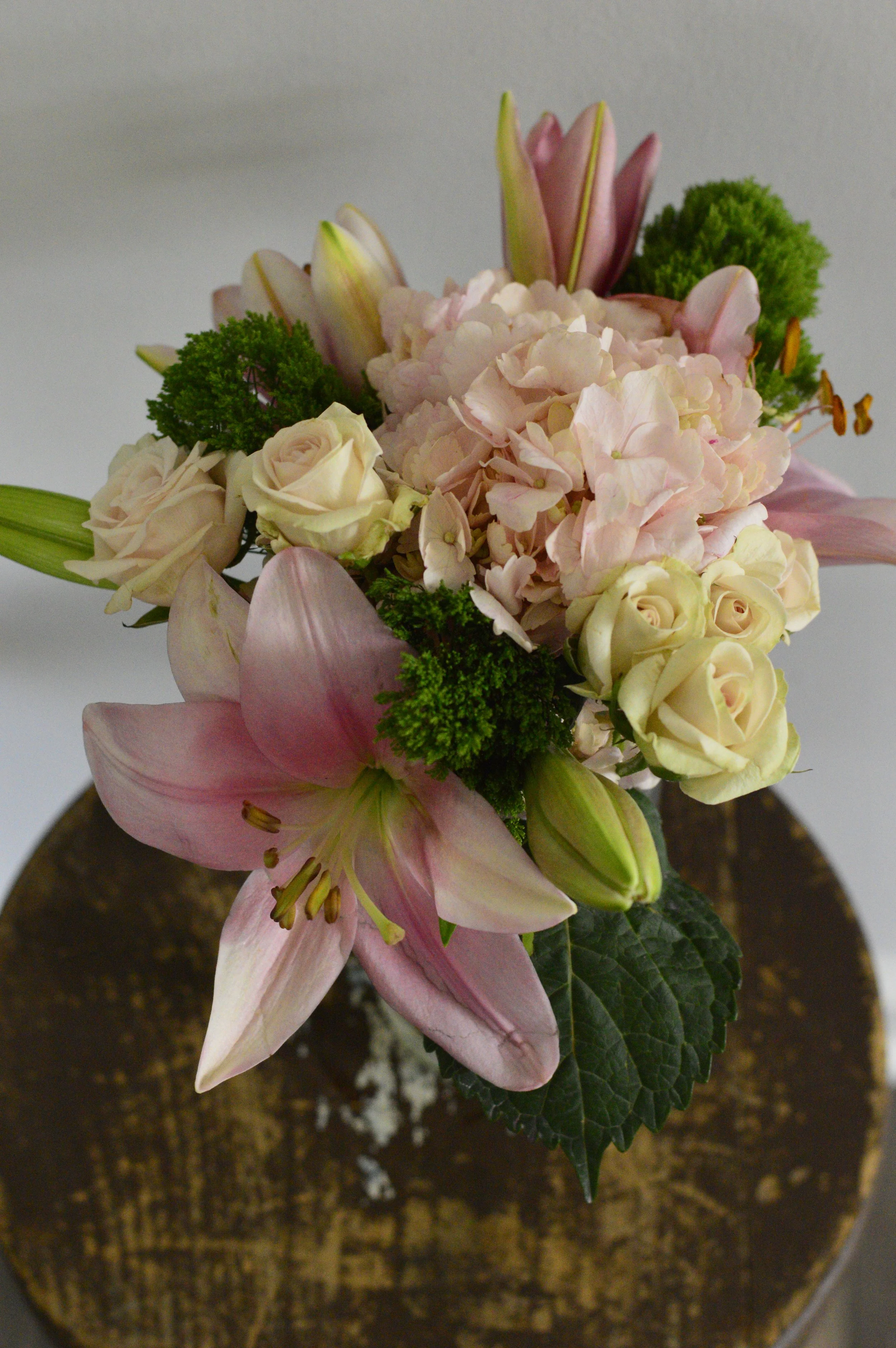 A bouquet of pink lilies, white roses, pink hydrangeas, and green foliage in a wooden vase.