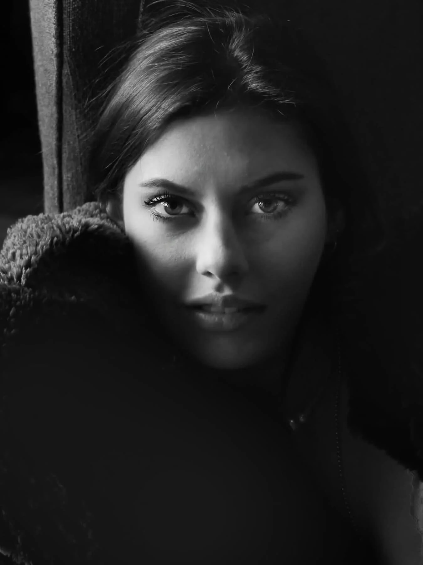 Black and white close-up portrait of a young woman with light-colored eyes, lying down and looking directly at the camera.