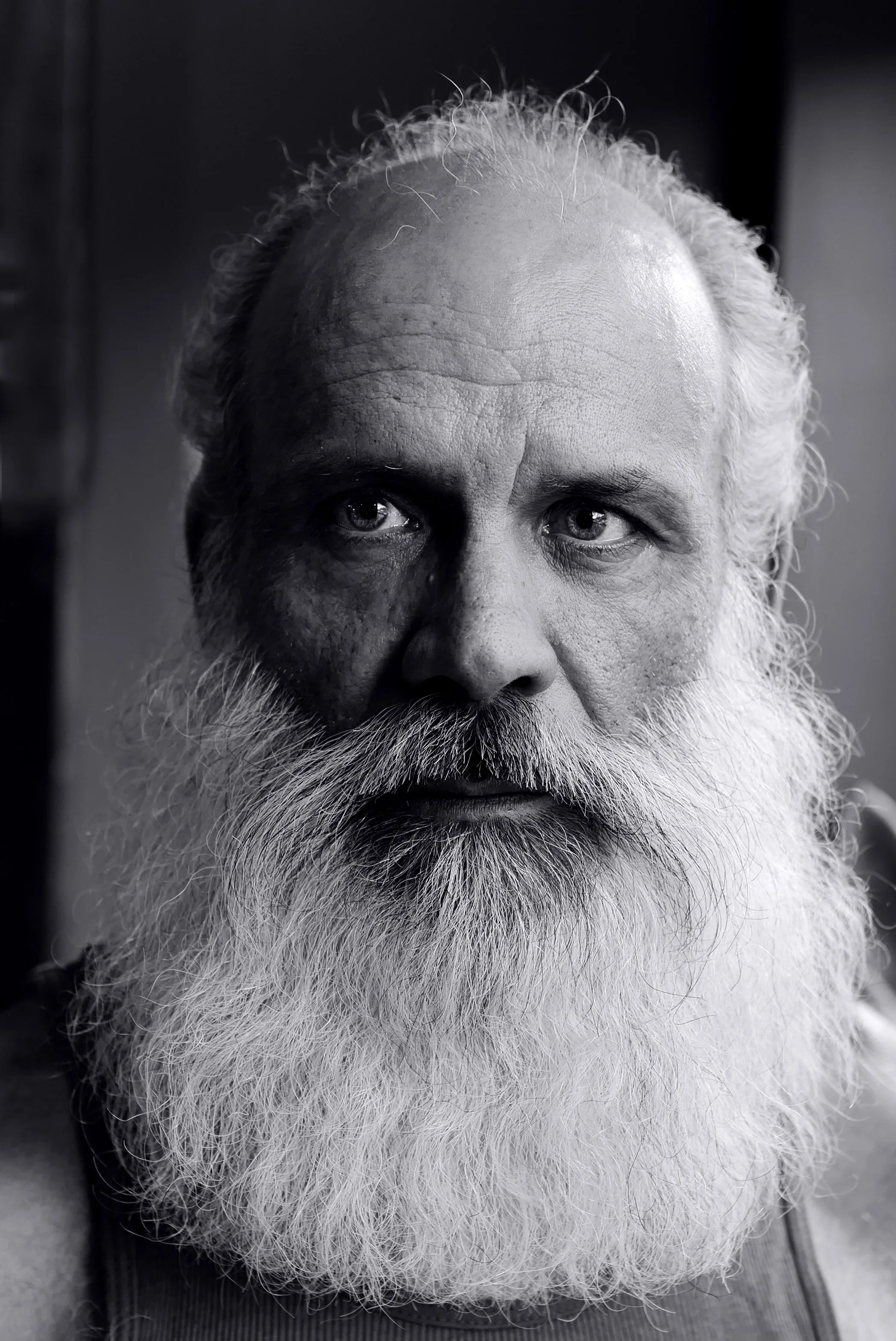 Close-up black and white portrait of a bearded man with white hair, intense eyes, and a serious expression.