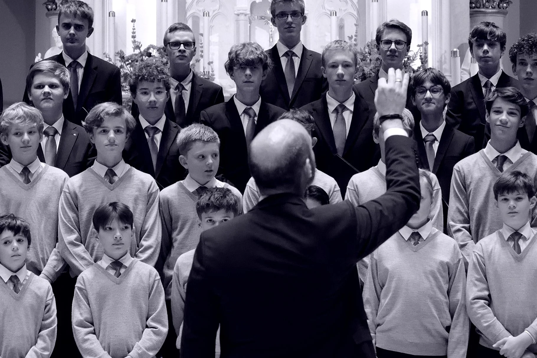 A choir of boys and young men singing in a church, with a conductor directing them.