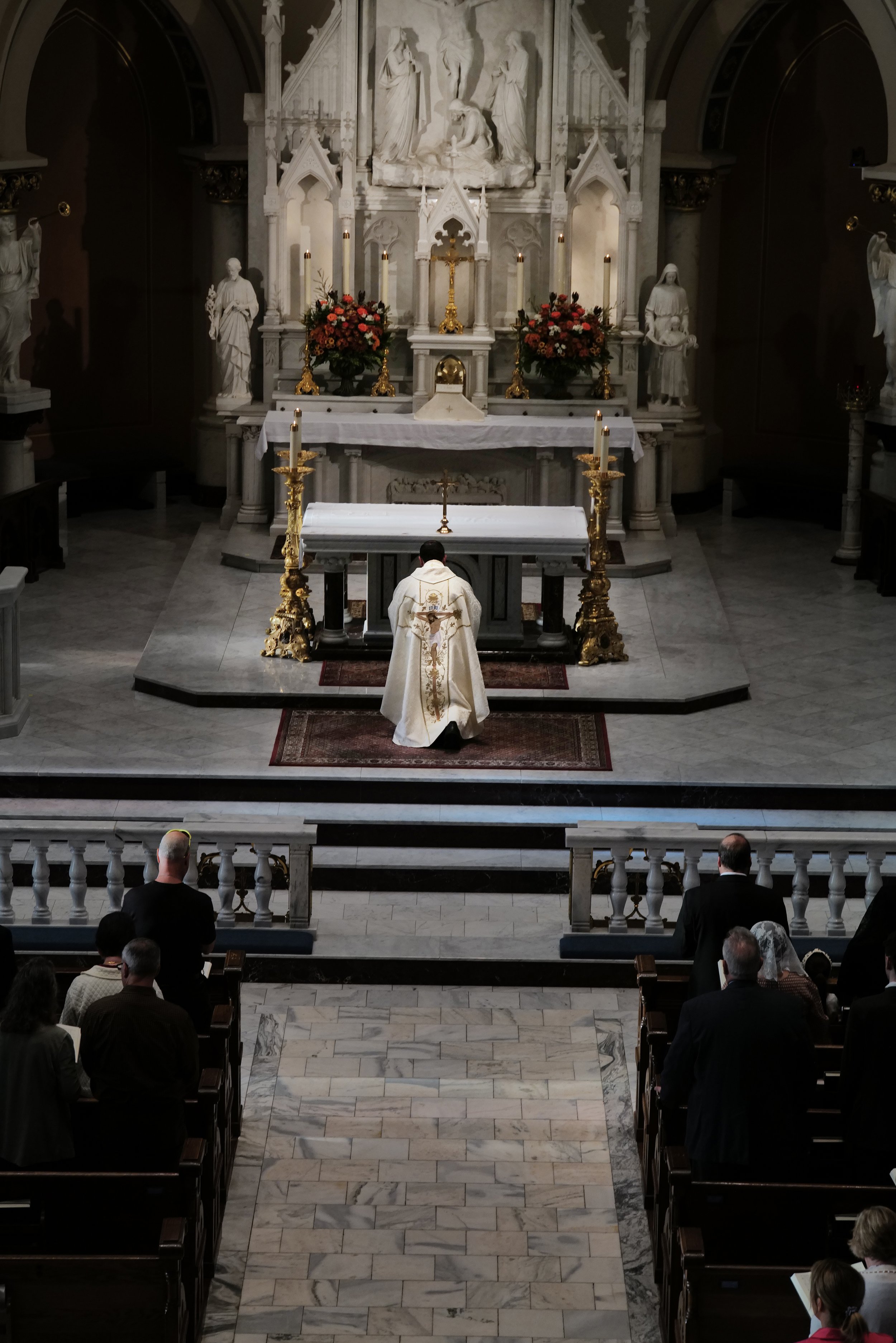 Priest standing at altar in a church during a religious ceremony with congregation seated and praying.