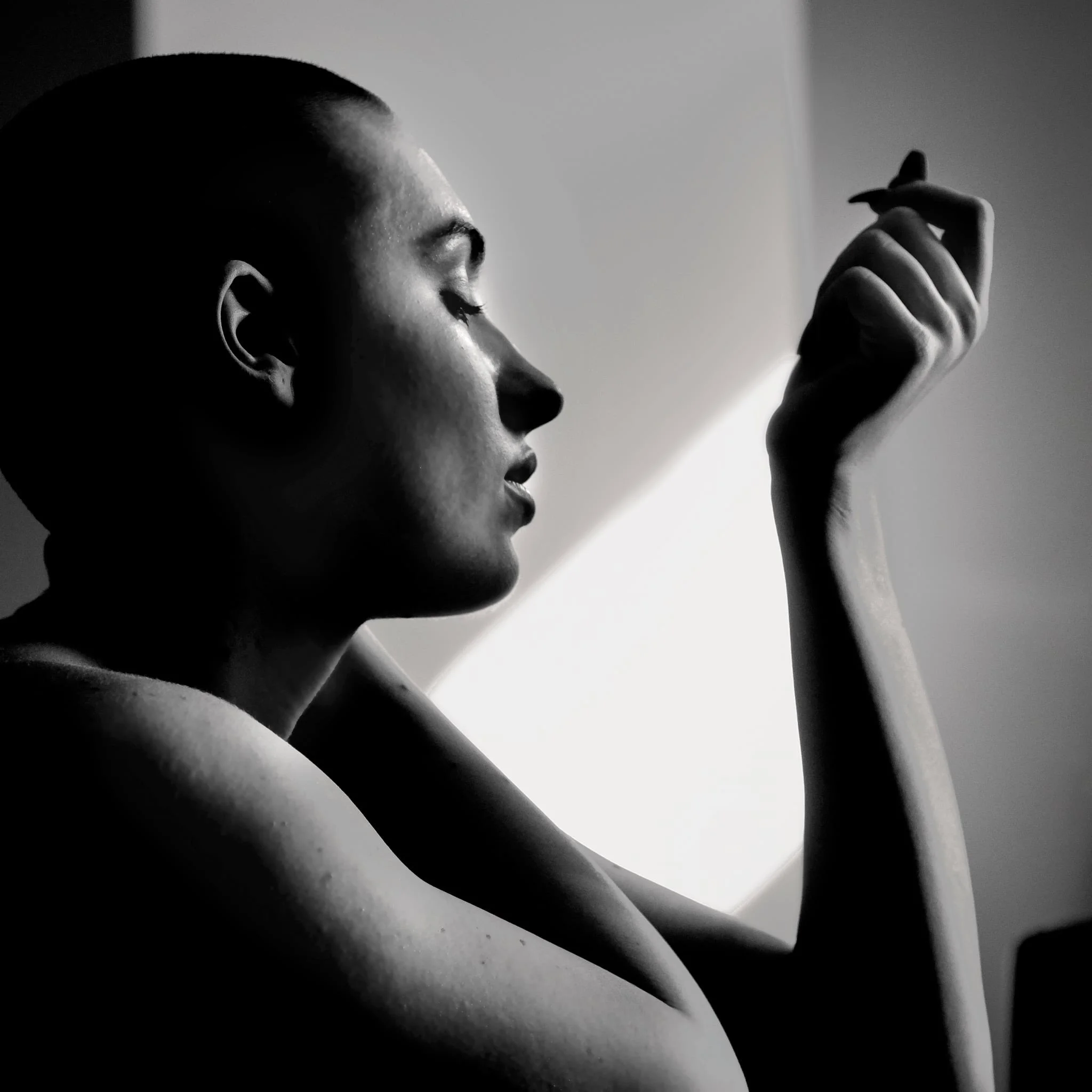 A black and white photograph of a woman with closed eyes and short hair, holding her arm up with her hand near her face.