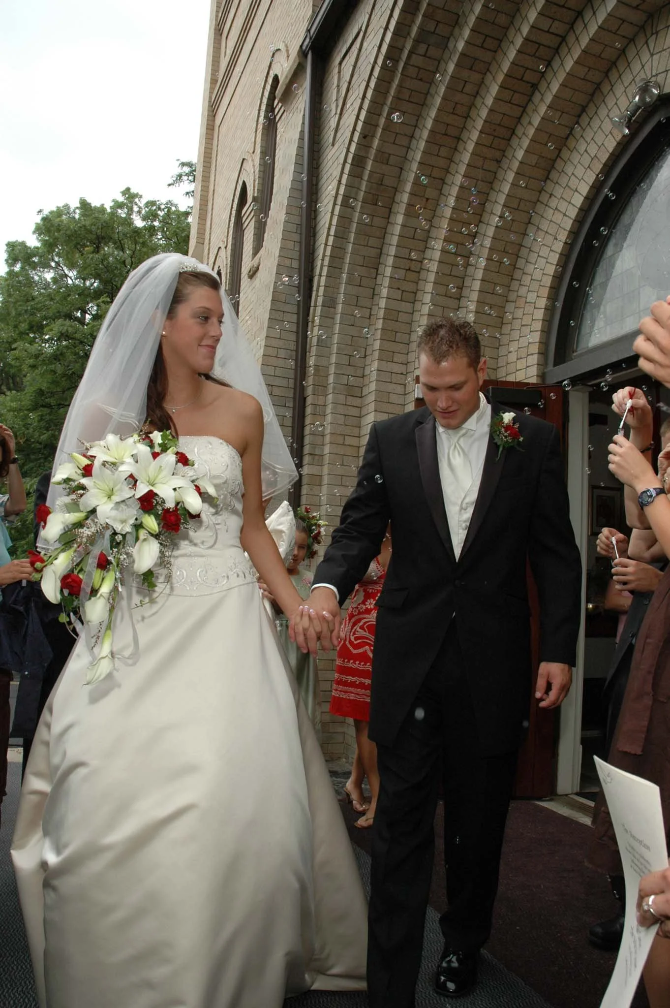 A bride and groom holding hands outside a church, surrounded by wedding guests.