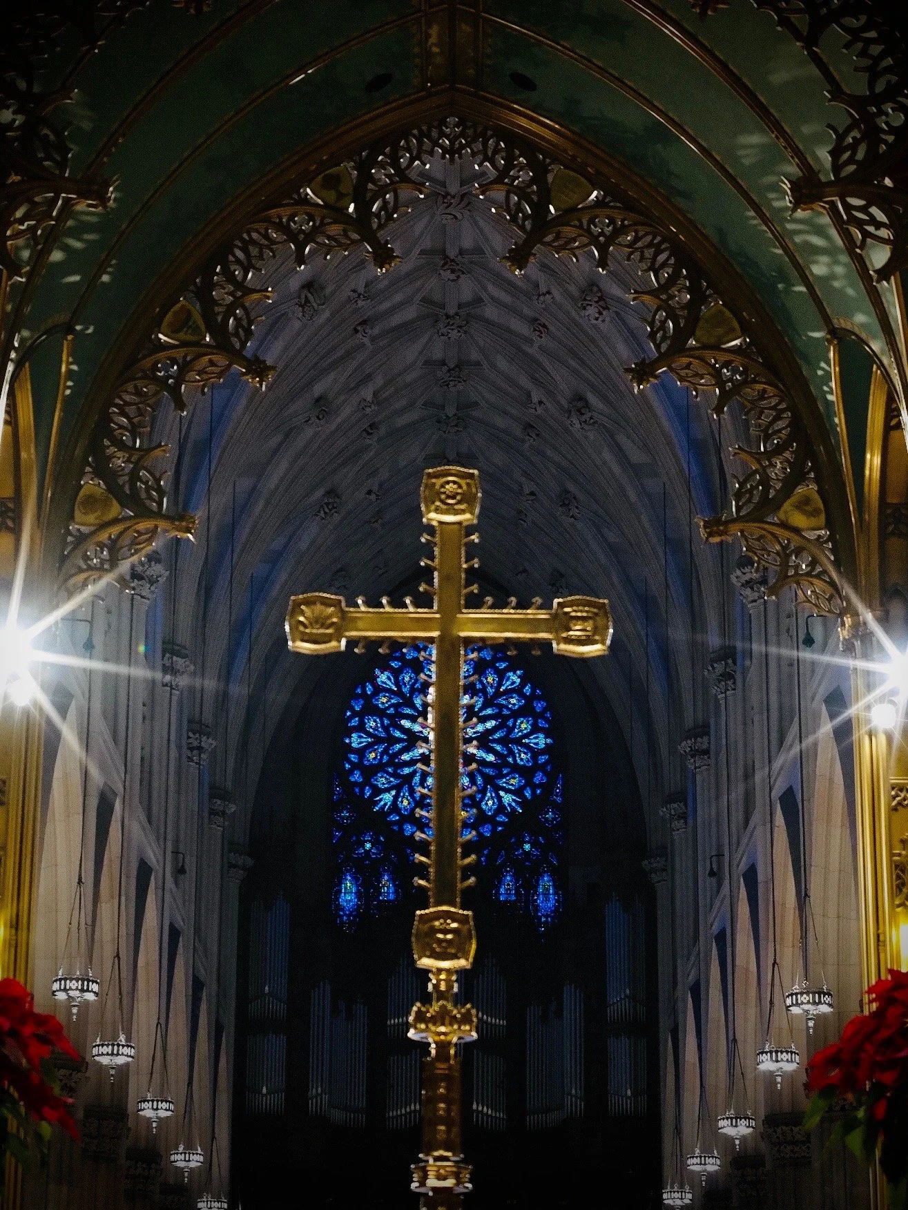 Gold cross inside a cathedral with stained glass windows and ornate architecture.