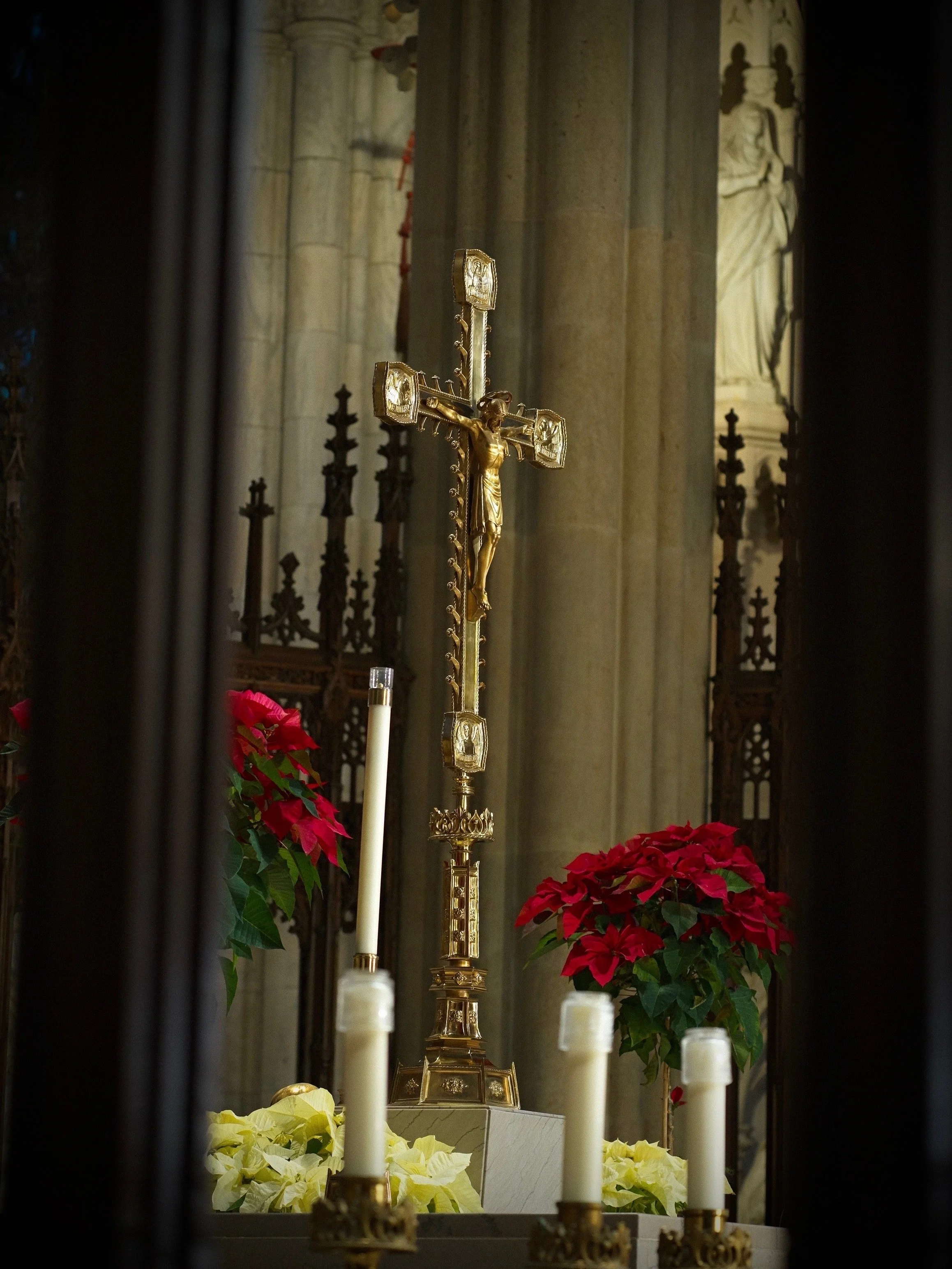 Religious altar with a gold crucifix, surrounded by red and white poinsettias, inside a church.