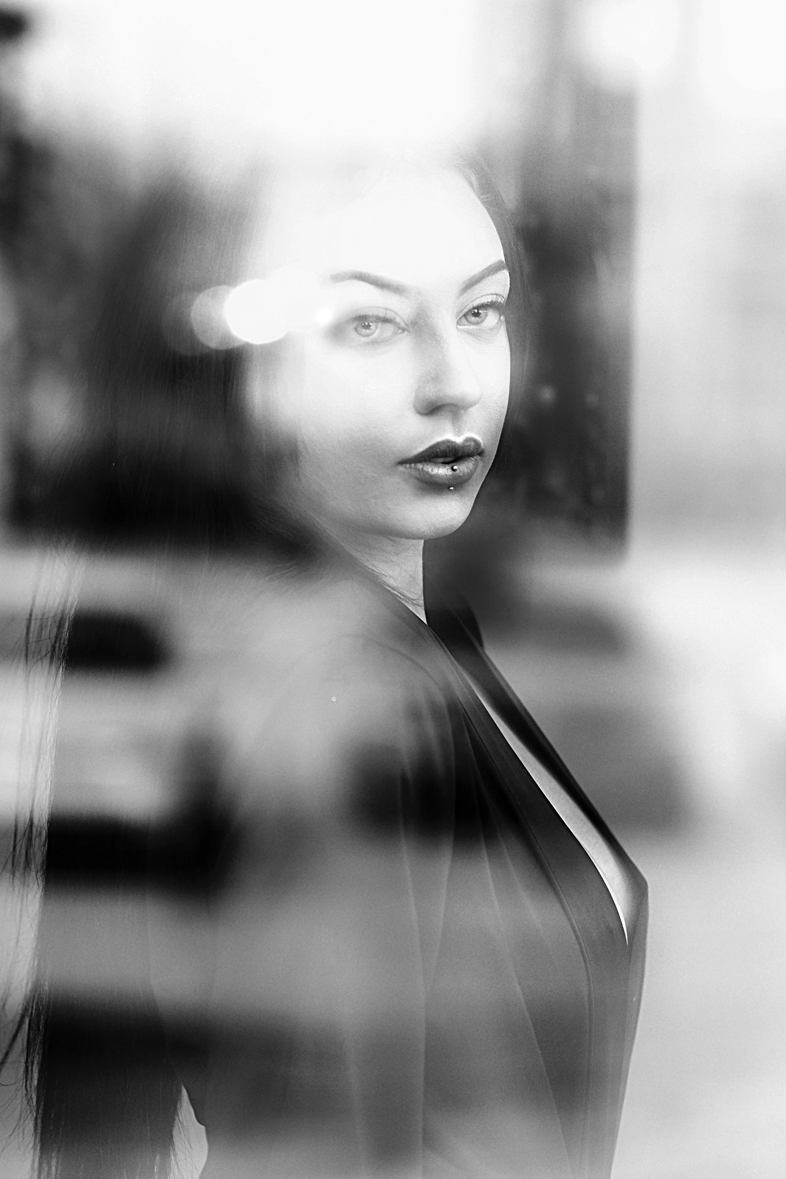 A black-and-white photo of a woman looking through a reflective surface, with her face partially obscured and soft sunlight highlighting her features.