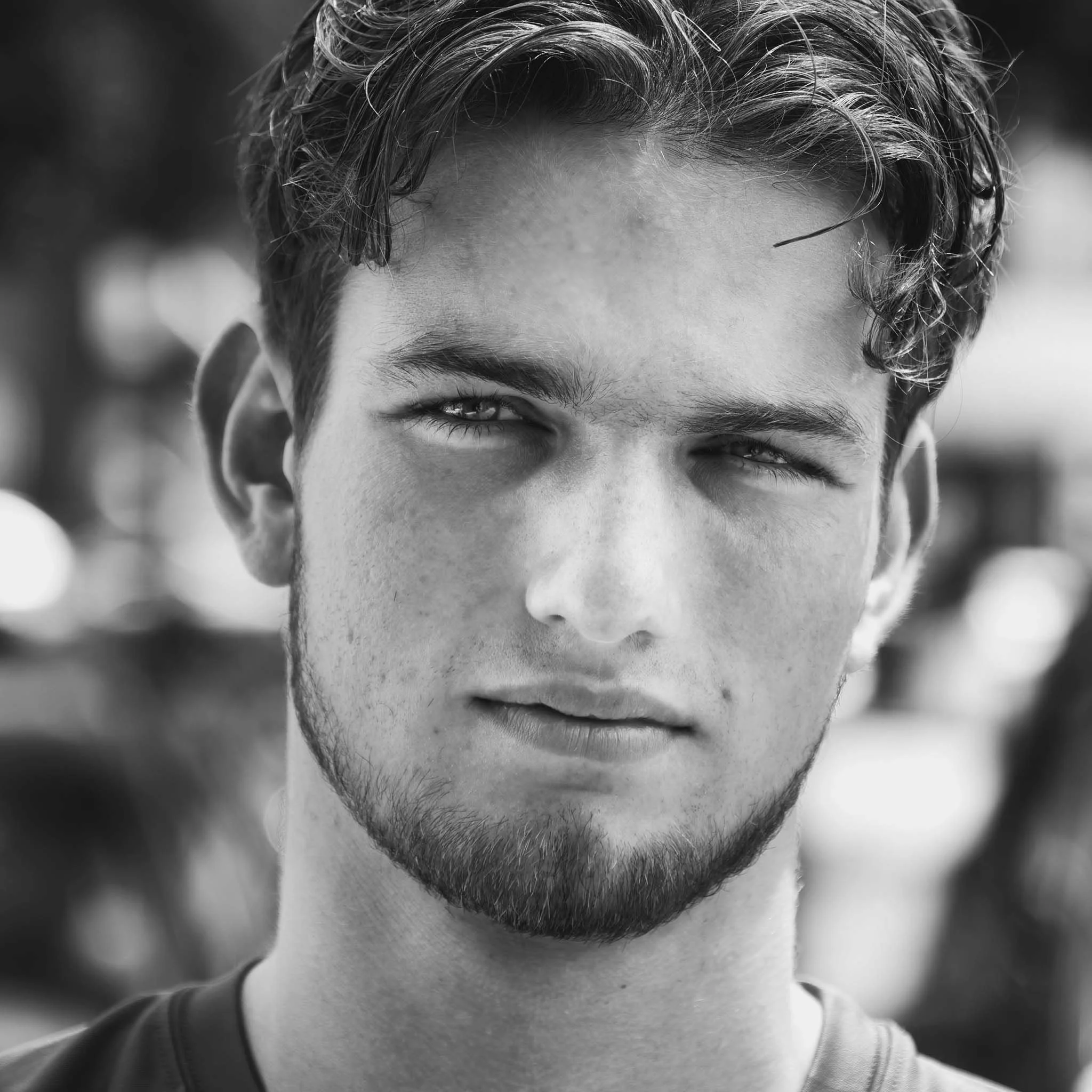 Close-up black and white portrait of a young man with short wavy hair and a beard, looking serious.