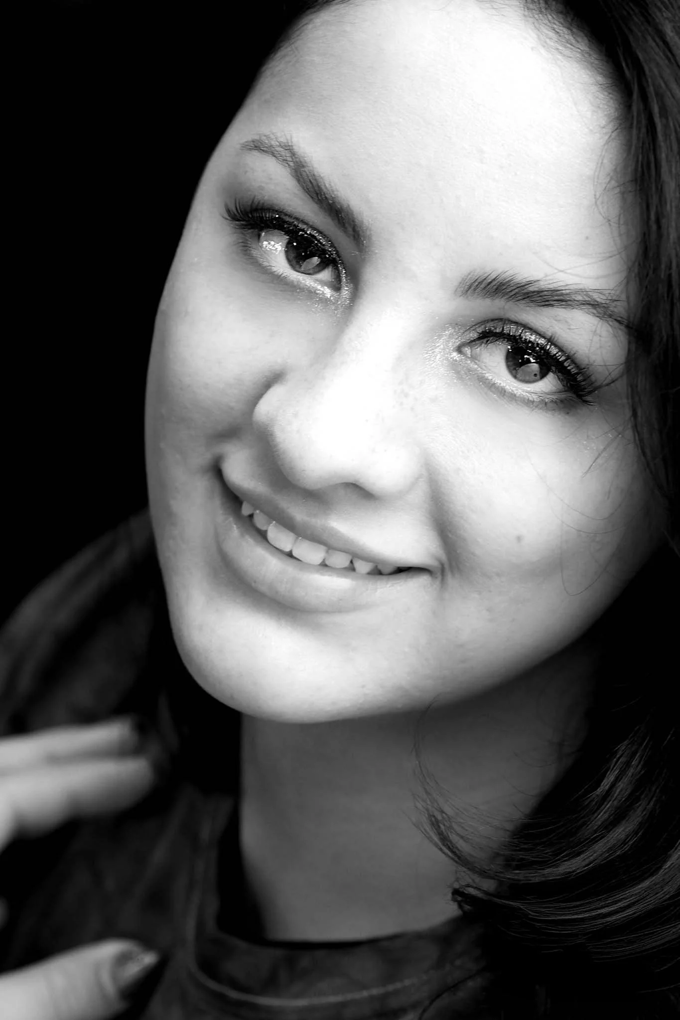 Close-up of smiling woman with dark hair, detailed facial features, and makeup, in black and white.