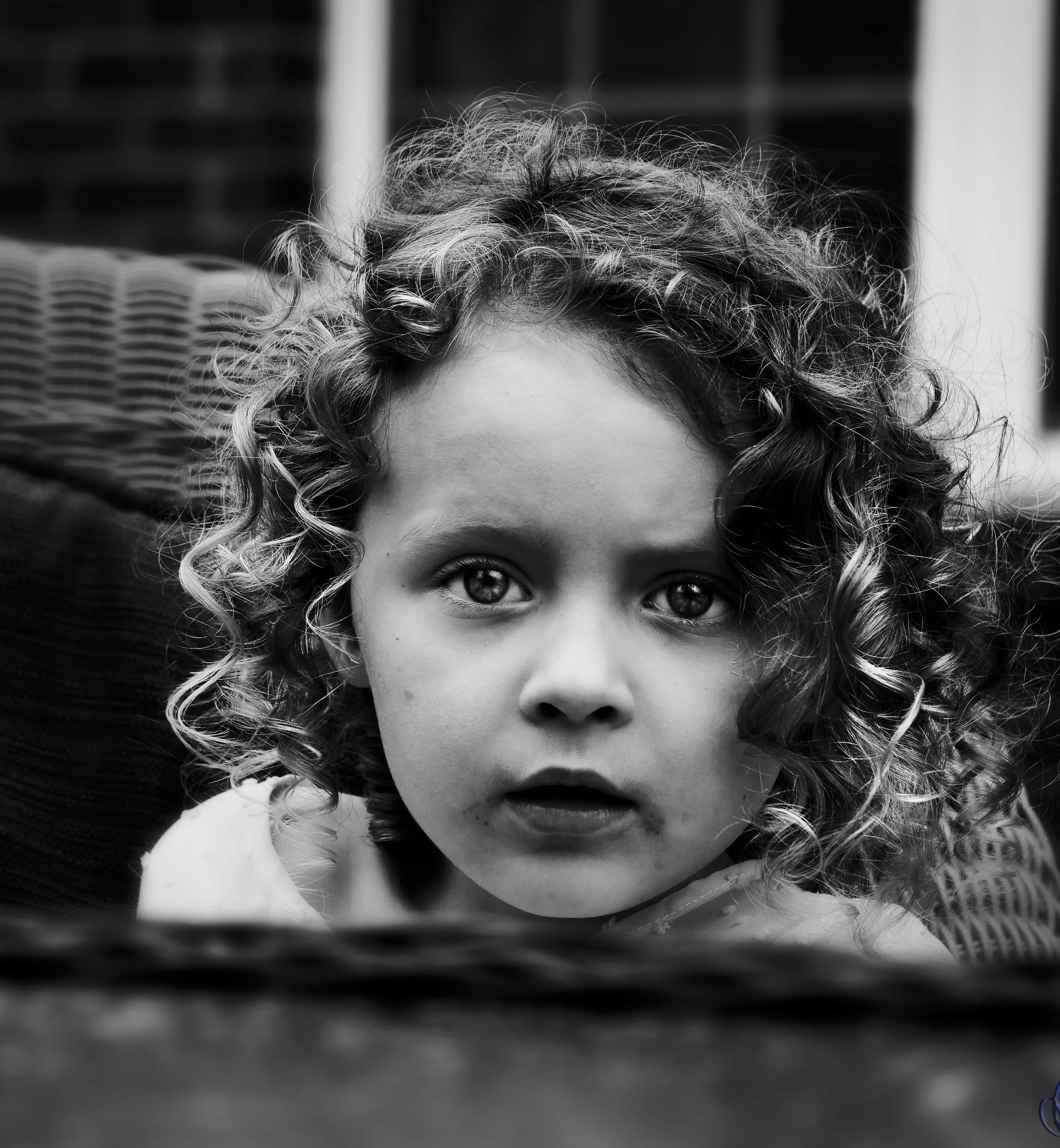 Black and white close-up portrait of a young girl with curly hair and intense eyes, looking directly at the camera.