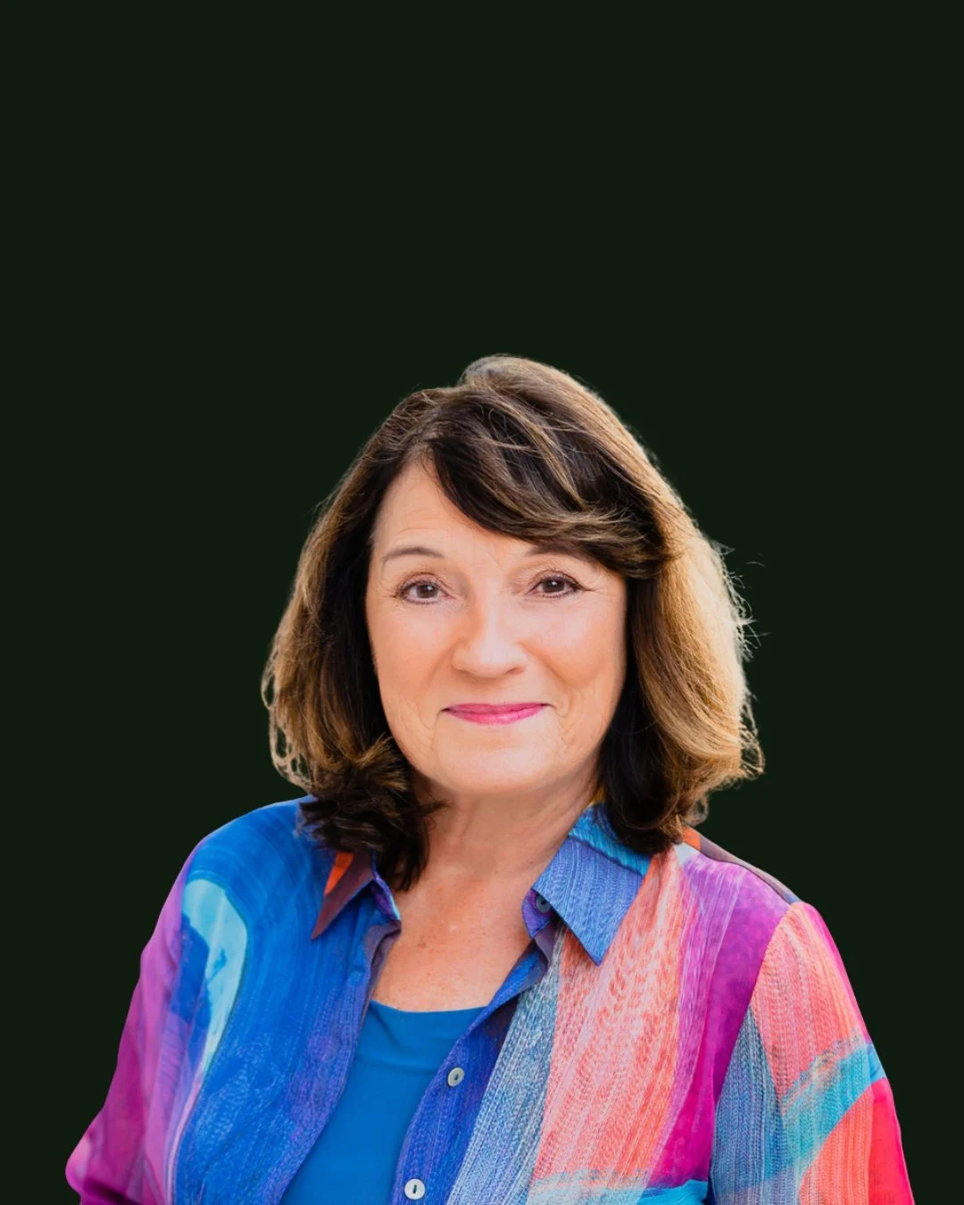 Portrait of a woman with shoulder-length brown hair, wearing a colorful, patterned blouse, smiling, with a dark background.