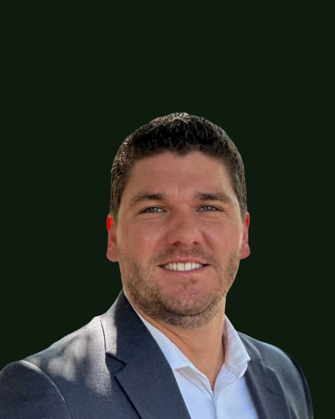 Headshot of a man smiling, wearing a gray suit and white shirt, with a dark green background.