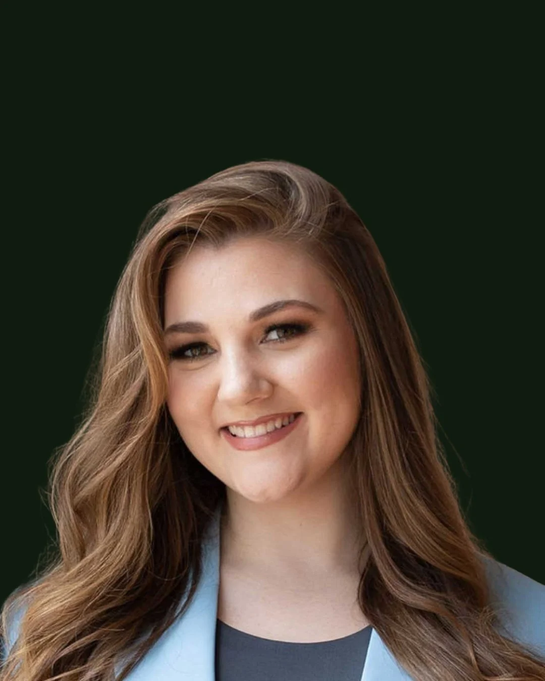 Portrait of a smiling woman with long, wavy brown hair, wearing a light blue blazer and black top, against a dark green background.