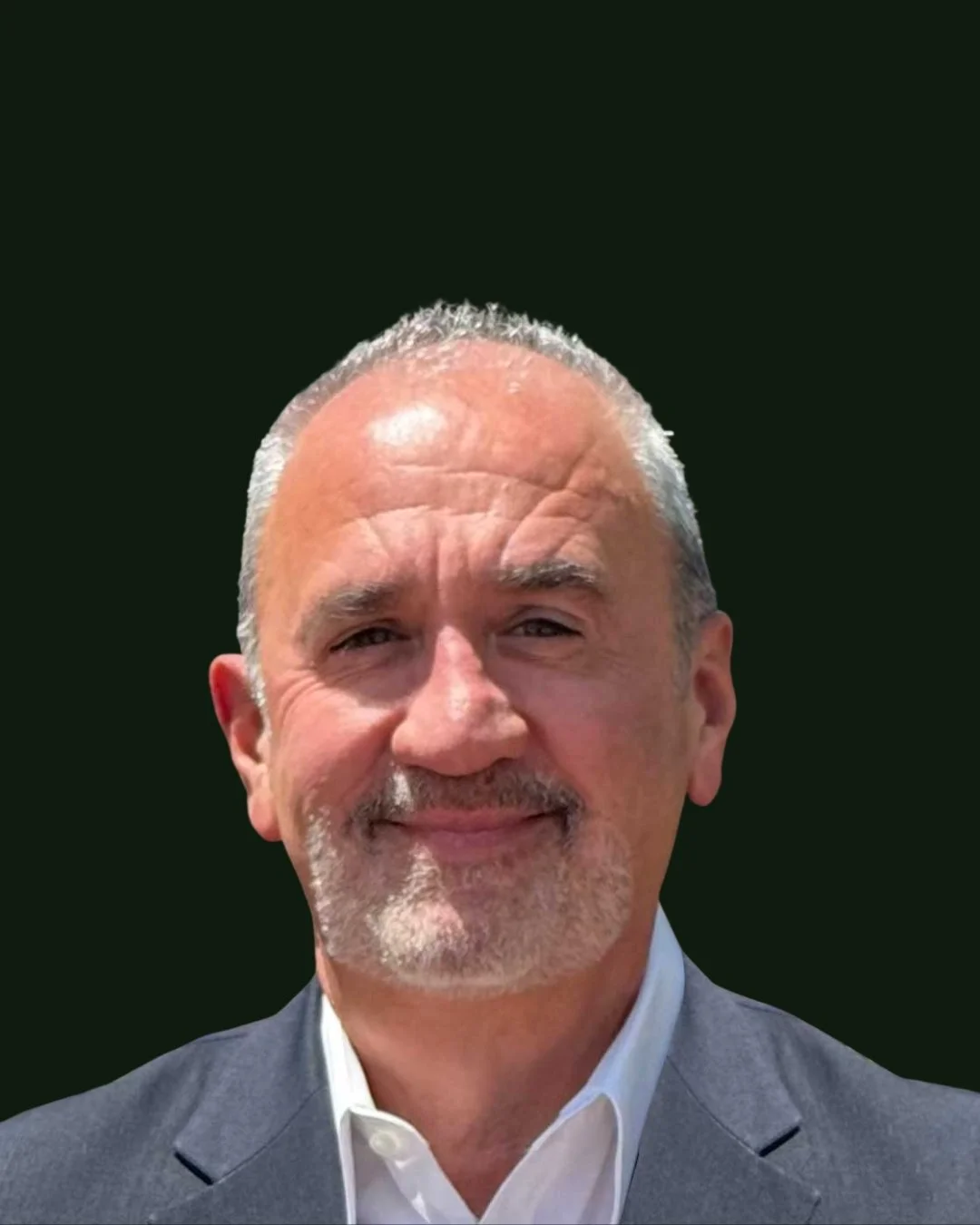 Close-up of a smiling mature man with grey hair, trimmed beard, wearing a grey suit jacket and white shirt, against a dark background.