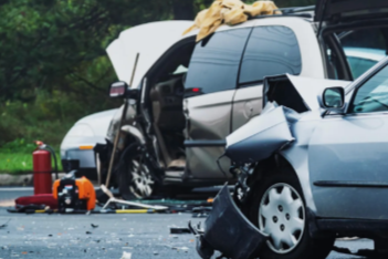 Car accident scene with damaged vehicles, including a silver sedan and black SUV, debris on the road, and emergency response equipment.