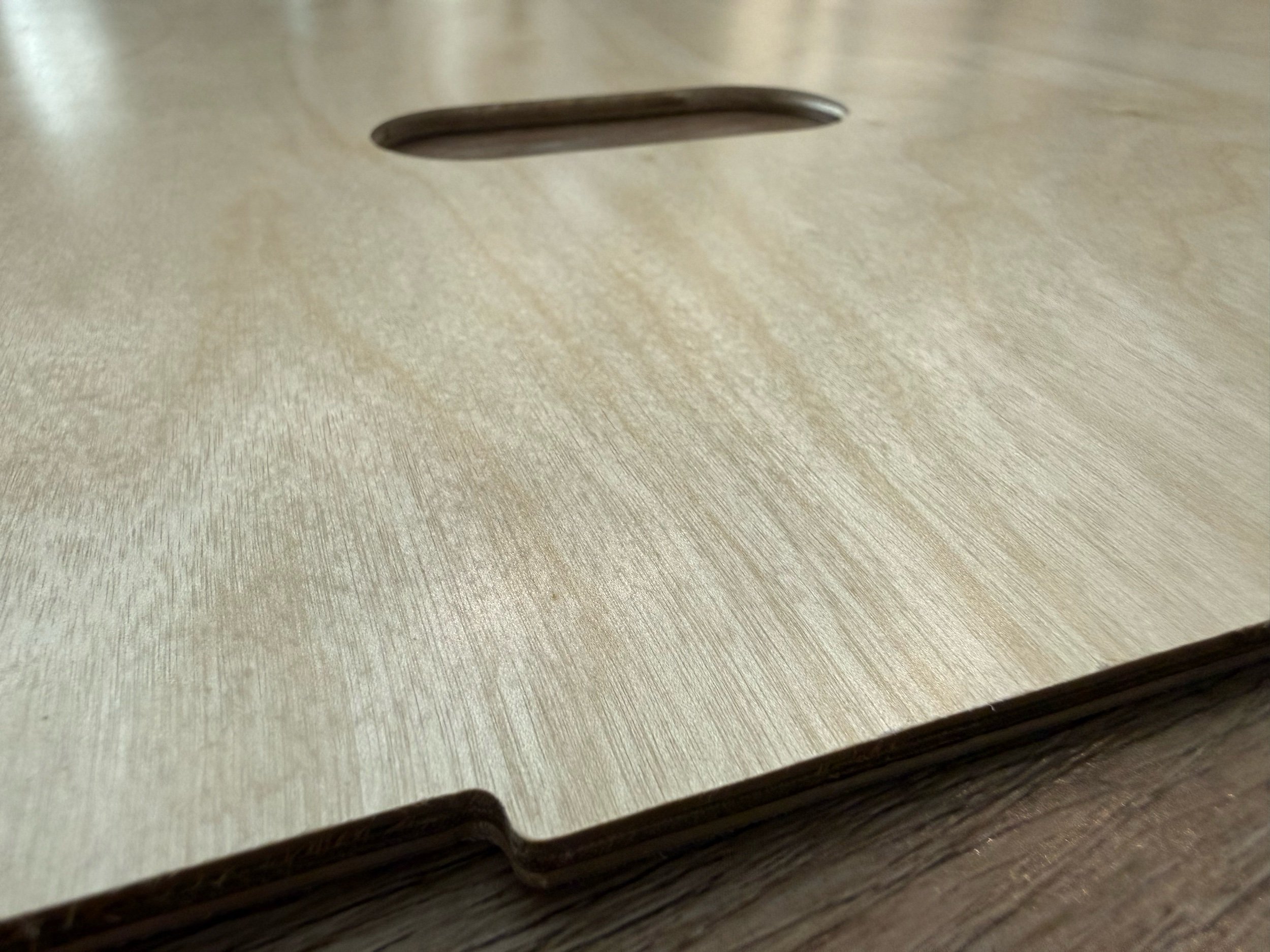 Close-up photo of a light-colored wooden surface with a cutout or slot, showing the texture and grain of the wood.