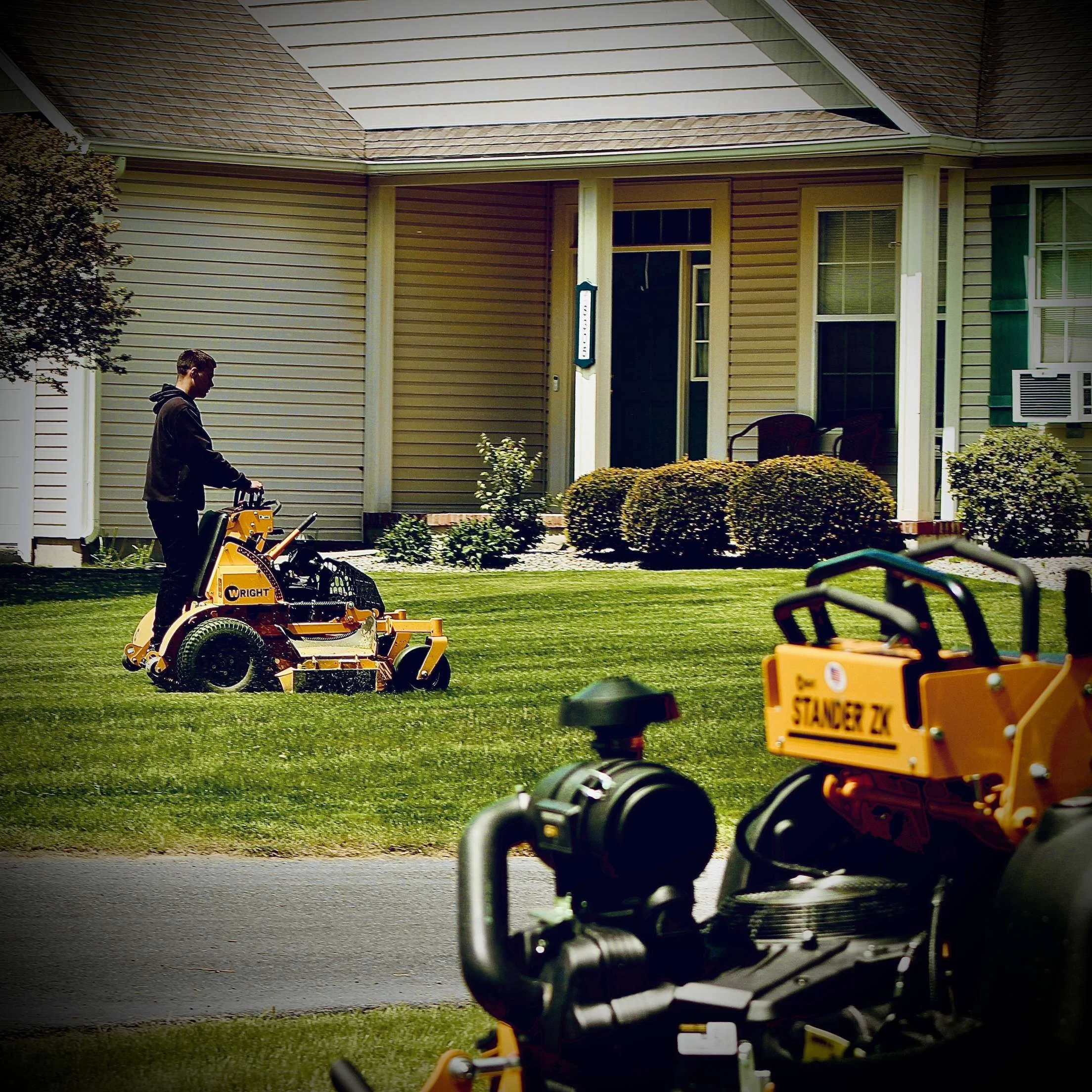 A person mowing the lawn in front of a house with a riding lawn mower.