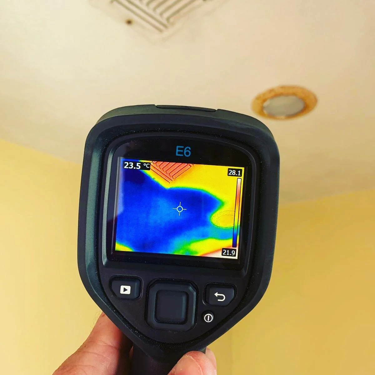 Thermal imaging camera displaying heat variations on a ceiling and wall, with temperature readings of 23.5°C and 28.1°C
