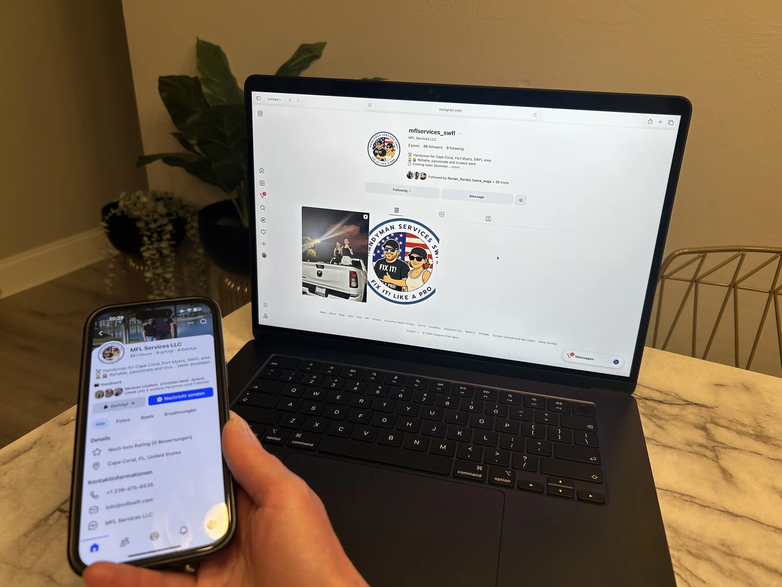 A person holding a smartphone displaying a business listing for MFL Services LLC in Cape Coral, Florida, with a laptop on a table showing the company's Instagram profile. In the background, there is a houseplant and a yellow wall.