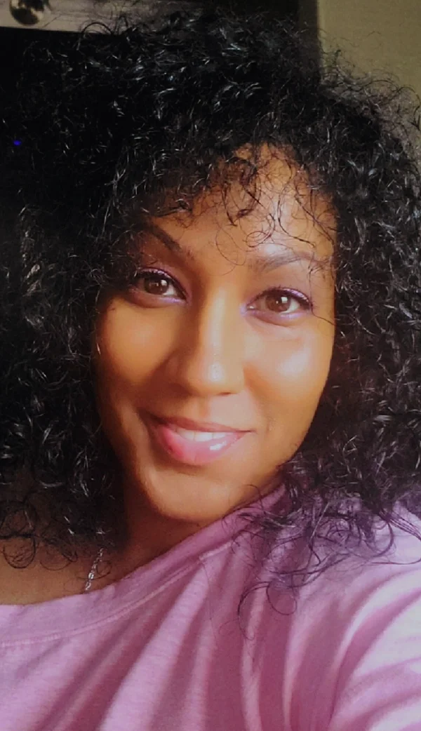 A woman with curly black hair smiling at the camera, wearing a pink top.