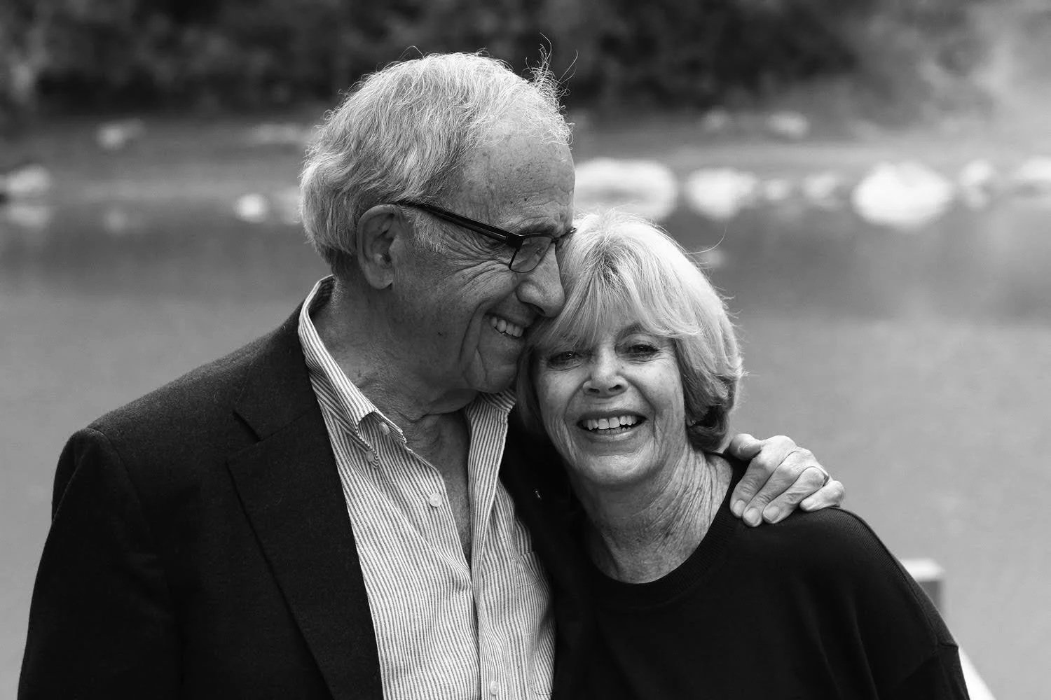 Ron and Myrna Ghitter smiling and embracing outdoors near a body of water in a black-and-white photo.