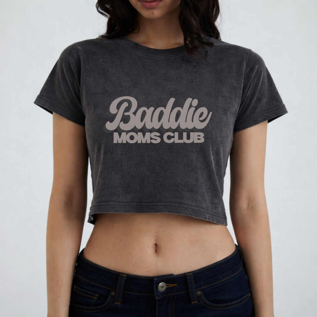 A woman wears a black cropped T-shirt with gray text that reads 'Baddie Moms Club' in a stylized font.